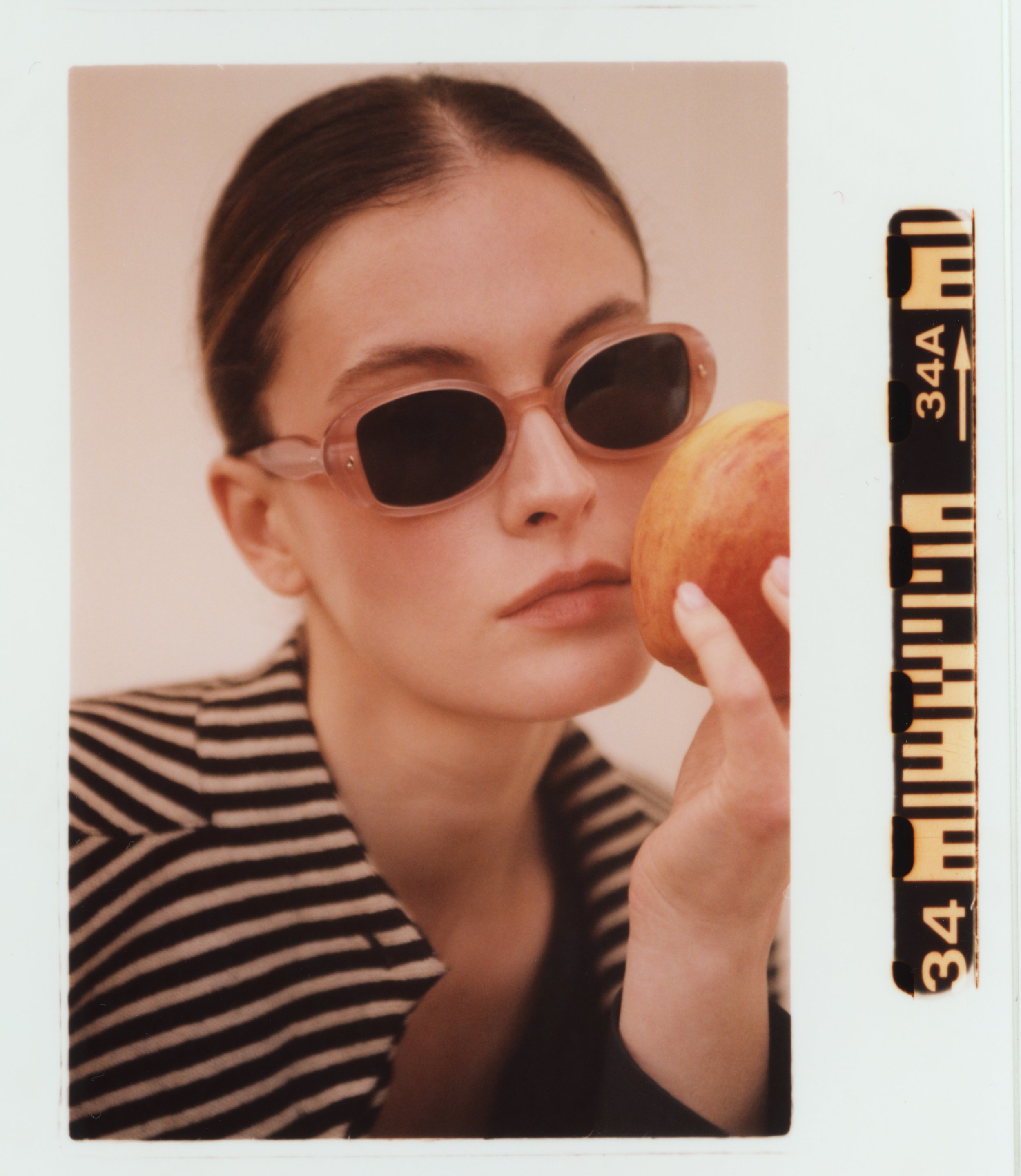 A woman with brown hair wearing pink sunglasses and a black and white striped shirt holding an apple.