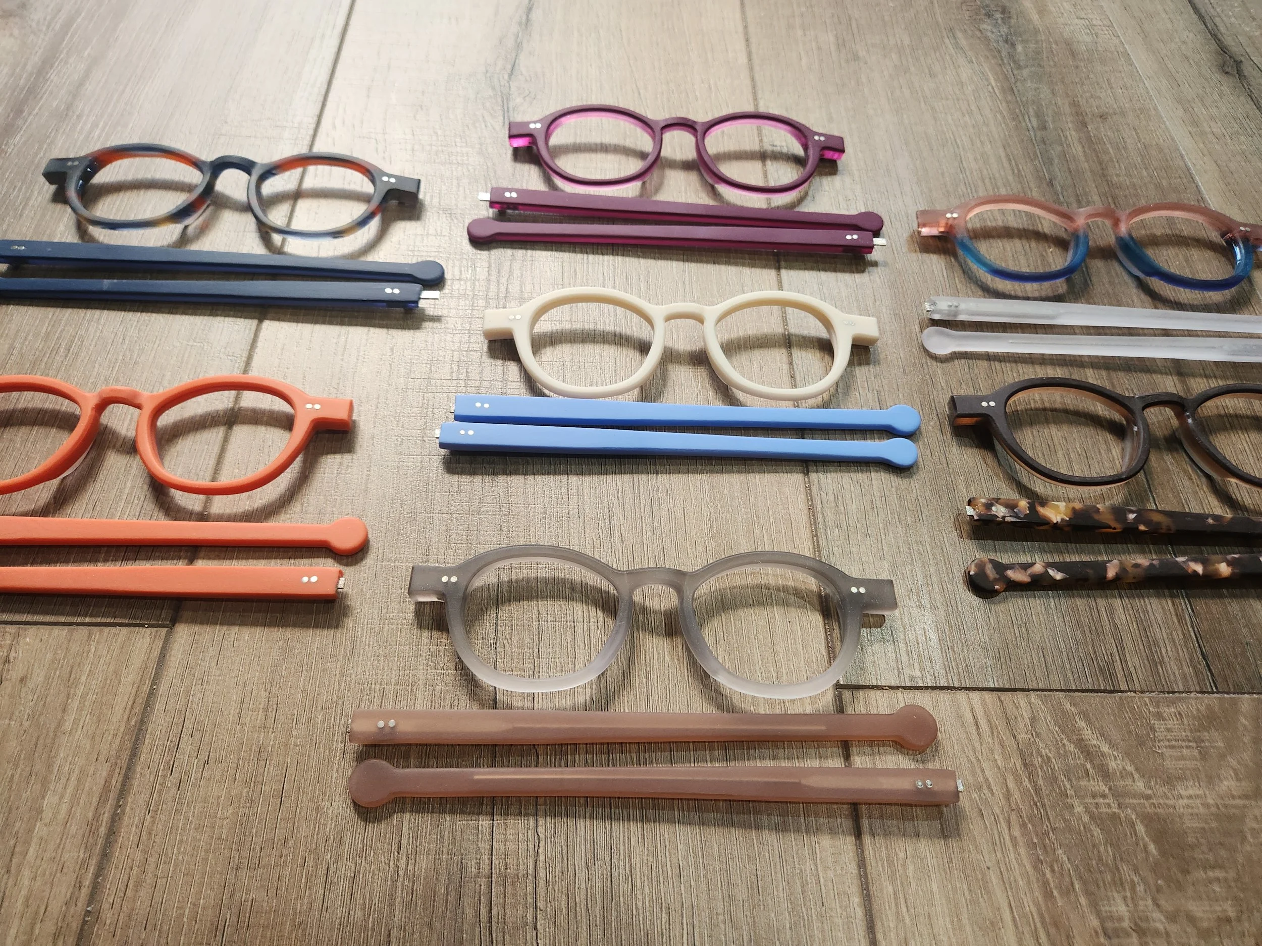 Various pairs of colorful eyeglasses and sunglasses arranged on a wooden surface.
