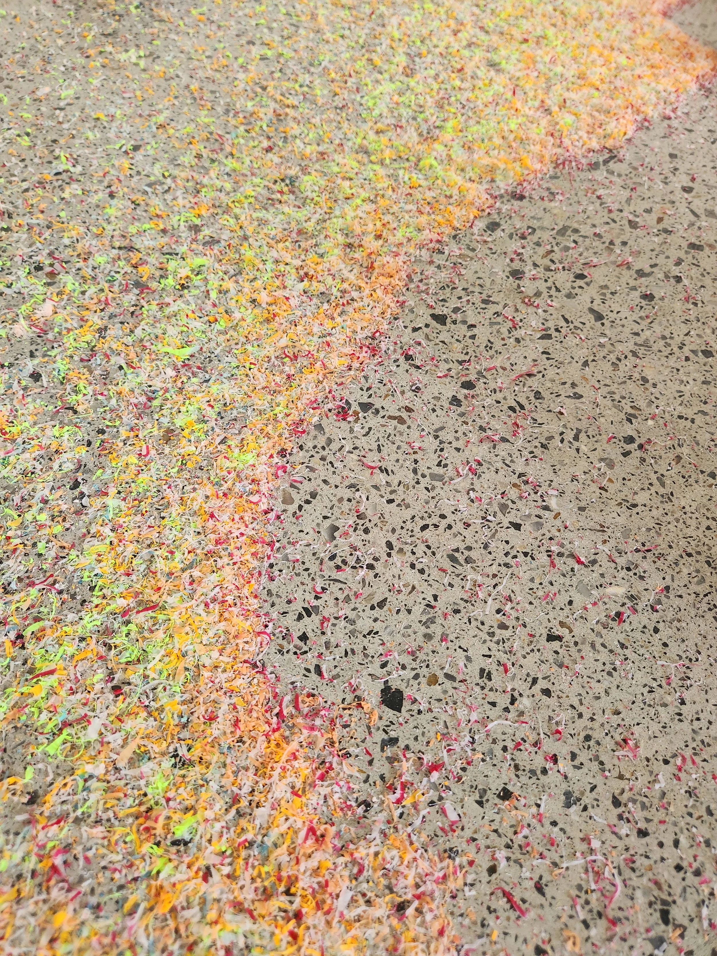 Colorful confetti and shredded paper scattered on a speckled concrete floor.
