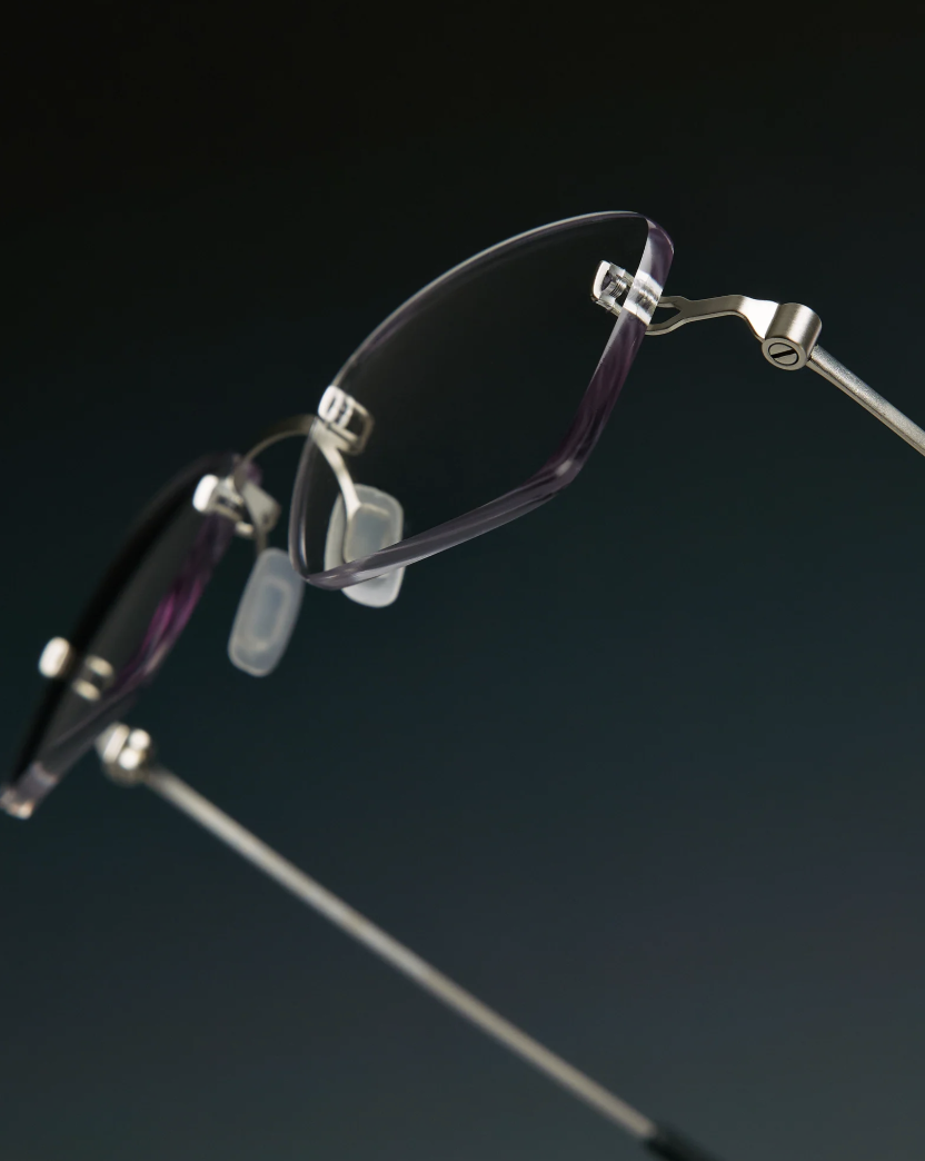 Close-up of a pair of eyeglasses with purple and black frames against a dark background.