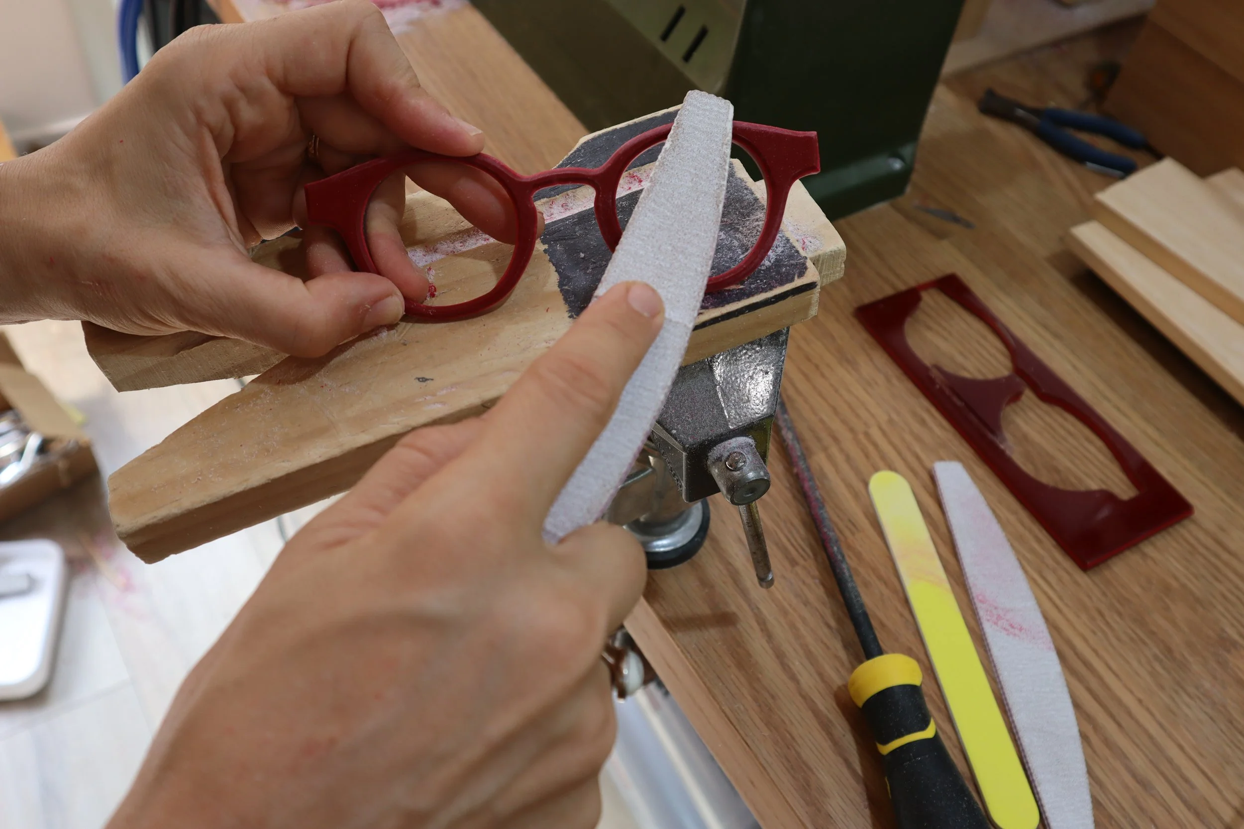 Person shaping a red plastic frame with a file on a workbench, woodworking tools in the background.