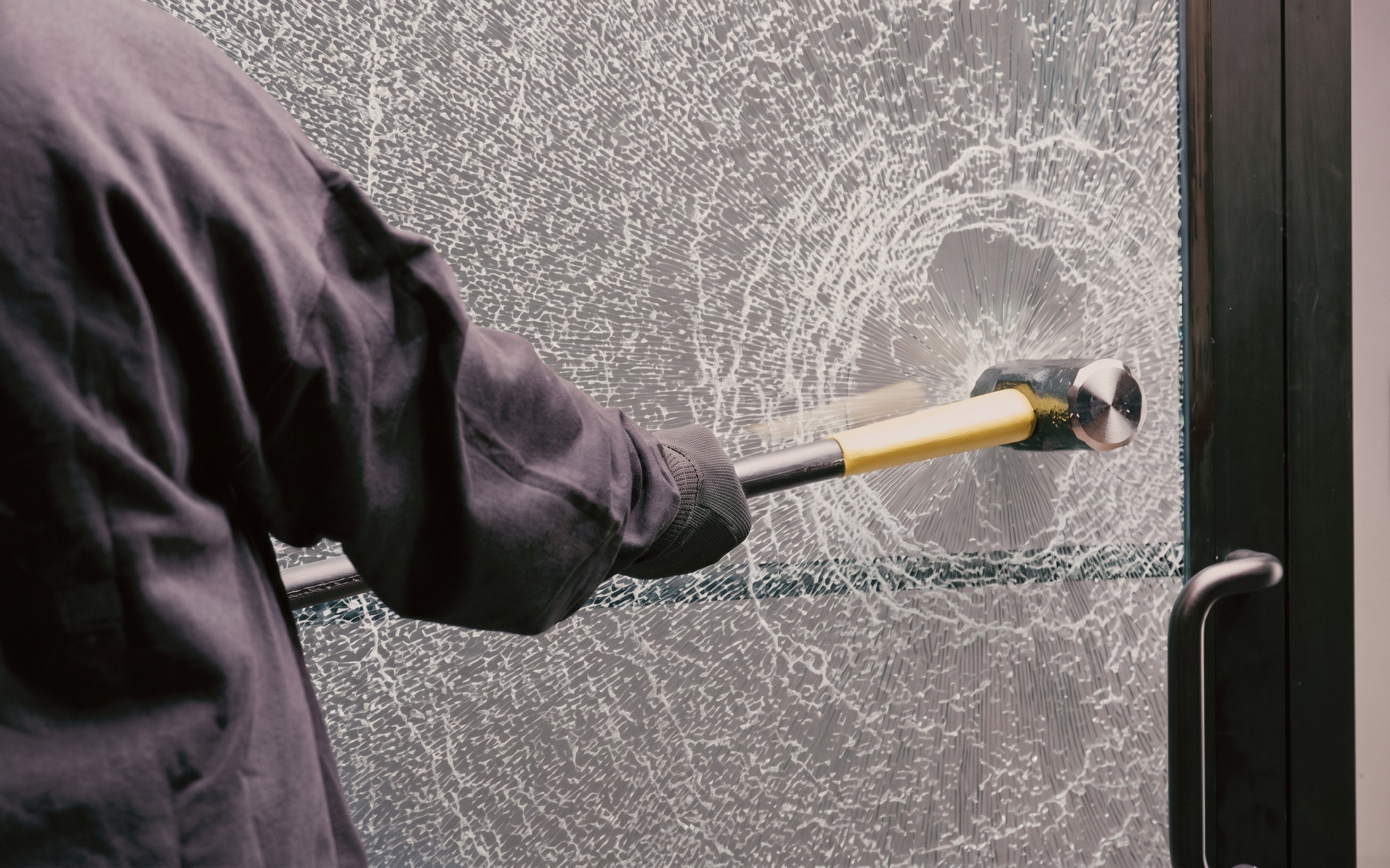Hammer striking glass protected by security window film showing shatter resistance