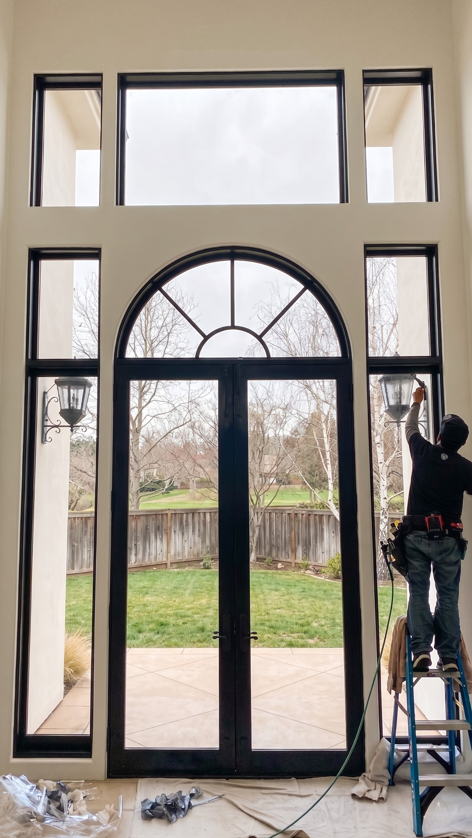 Technician on ladder installing security window film on large residential glass doors