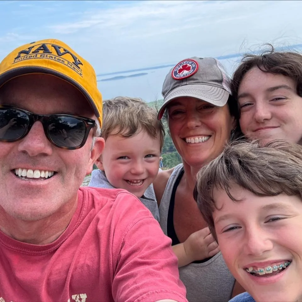 Family taking a selfie outdoors near a body of water, all smiling and enjoying the moment.