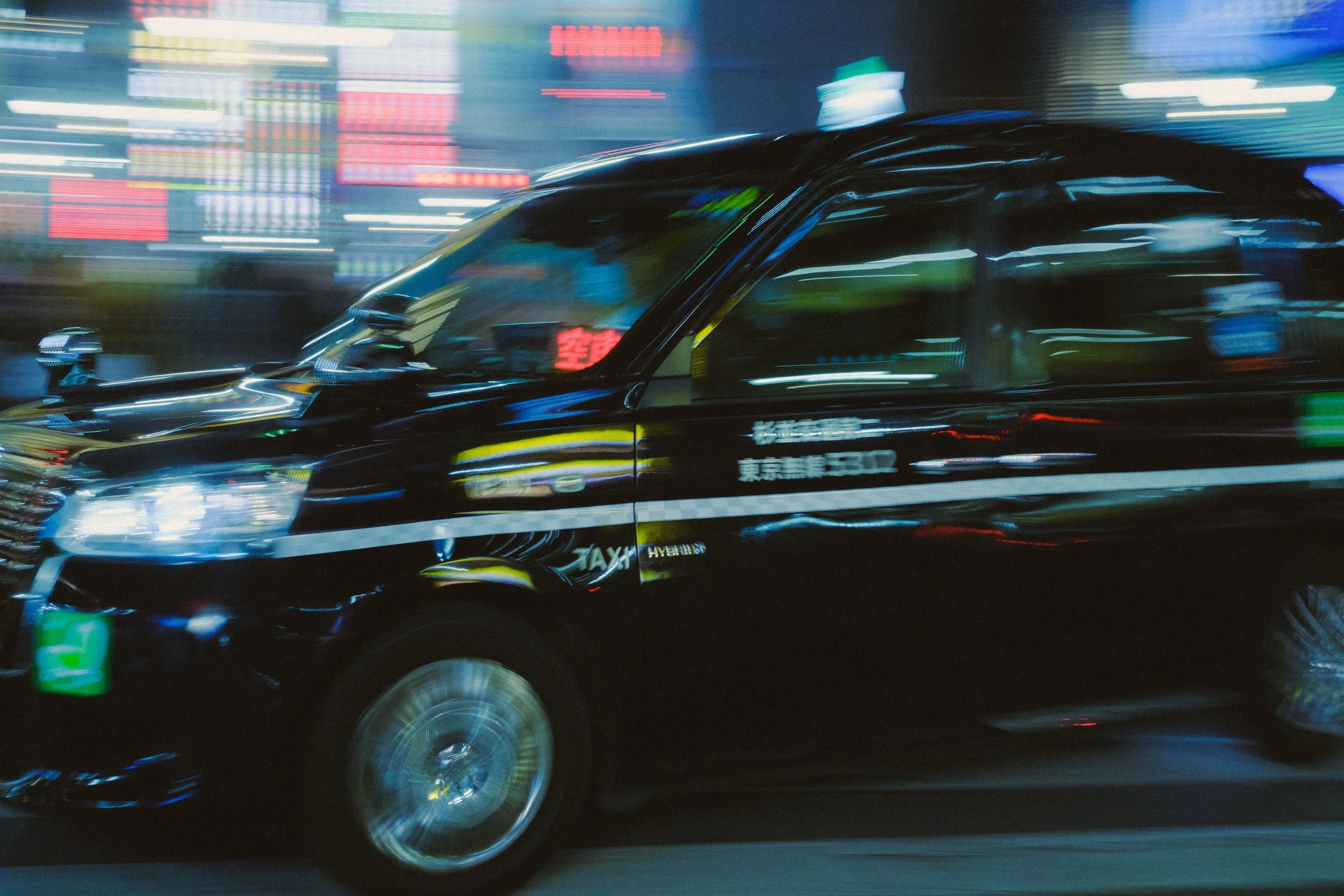 Moving black taxi cab with blurred city lights in the background at night.