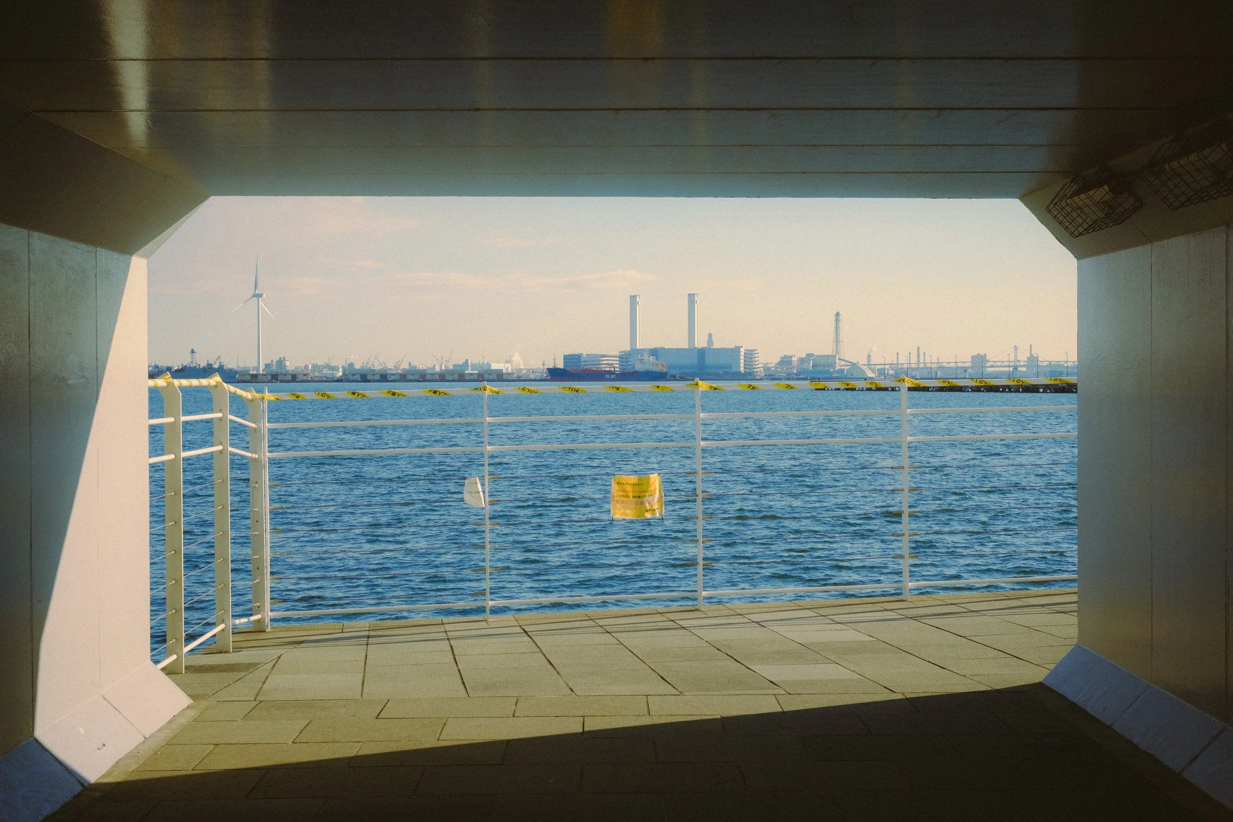 View of industrial cityscape and water seen through a large, rectangular opening in a wall or structure from inside a building or tunnel.