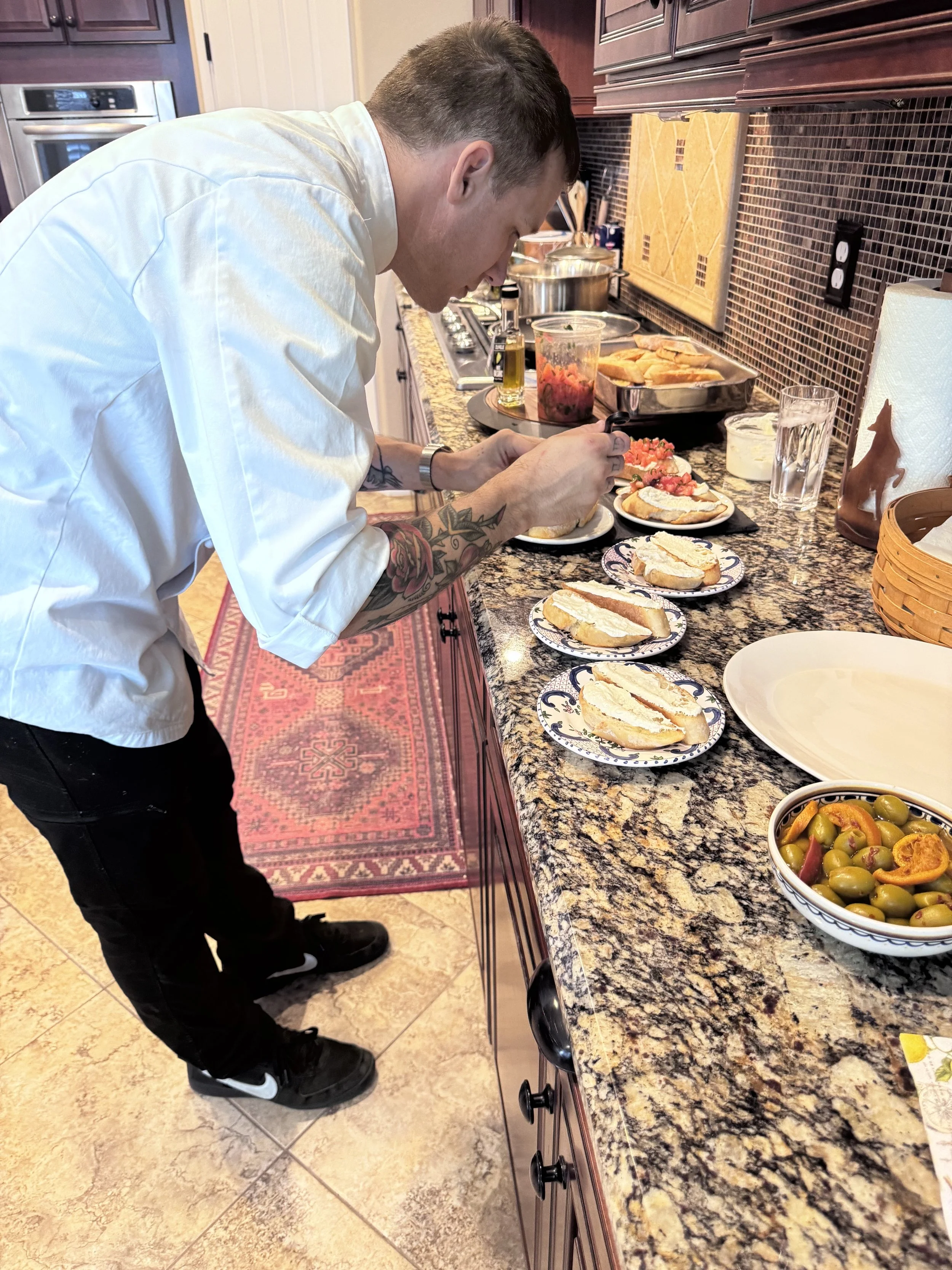 Chef Mitch Bell plating individual bruschetta and burrata appetizers on a home kitchen counter for a private dinner.