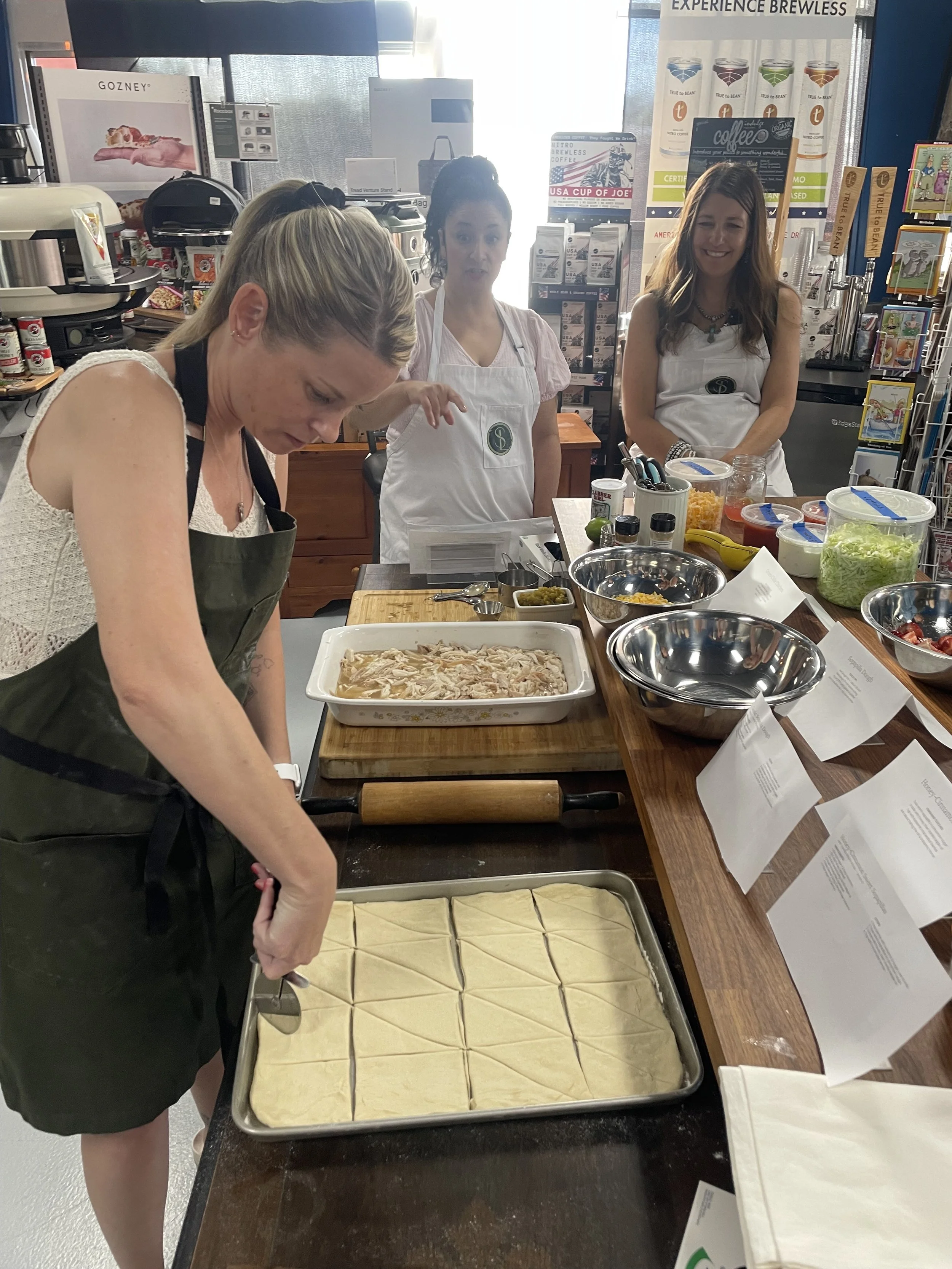 Guests scoring and portioning dough during a cooking class, with prep bowls and ingredient labels laid out on a work table.