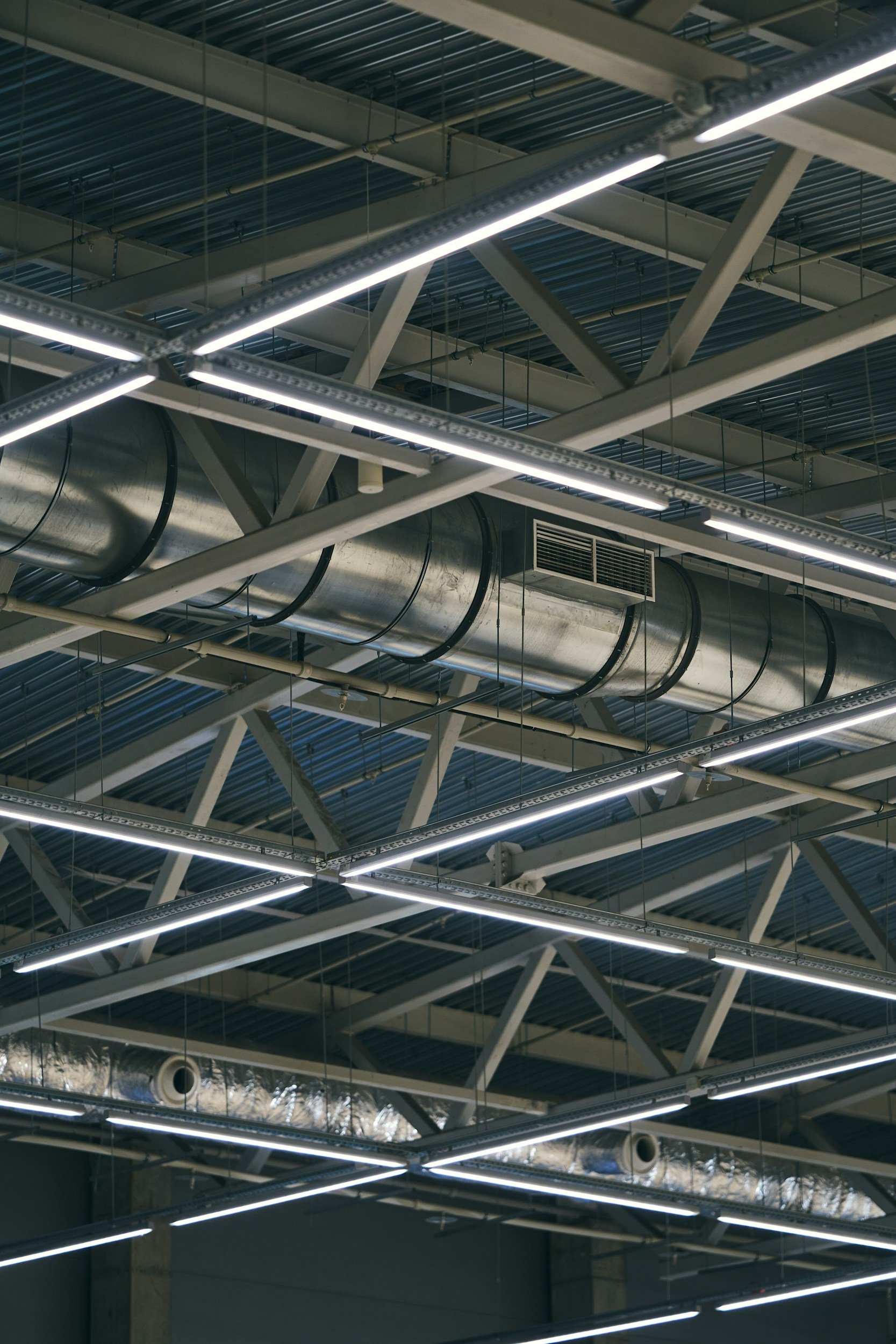 Ceiling with exposed structural beams, ductwork, and fluorescent lighting fixtures in an industrial or commercial building.