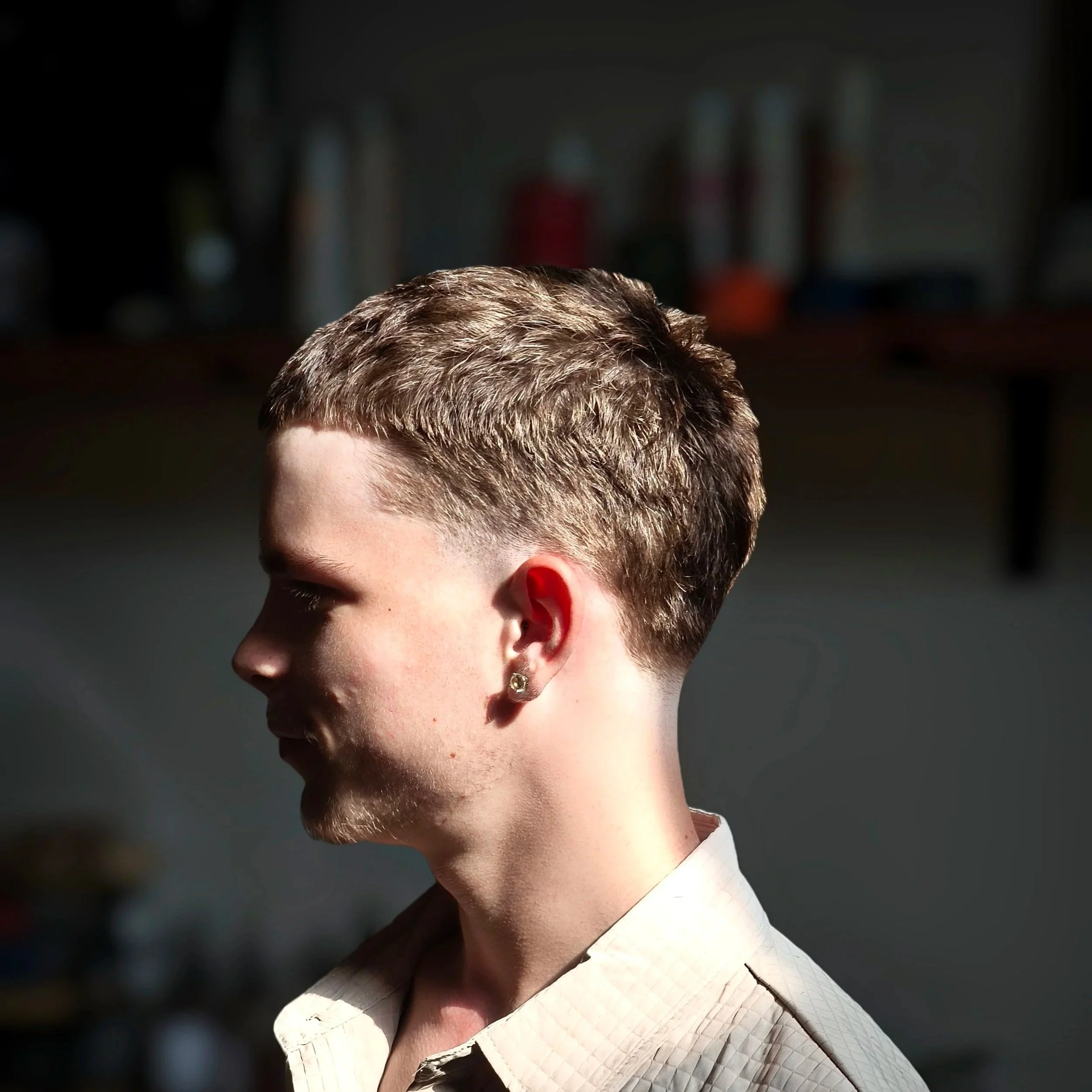 Close-up of a person's head with short, reddish-brown hair and an earring, wearing a white textured blazer.