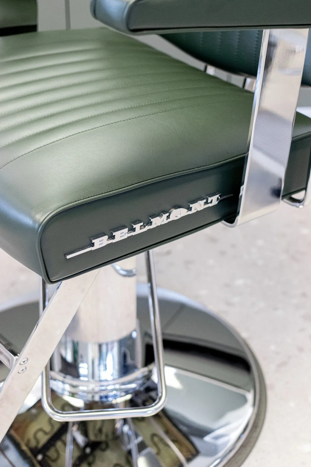 Close-up of a vintage green leather medical or dental chair with the brand name 'BEEMAN' in chrome letters, supported by chrome metal parts and wheels.