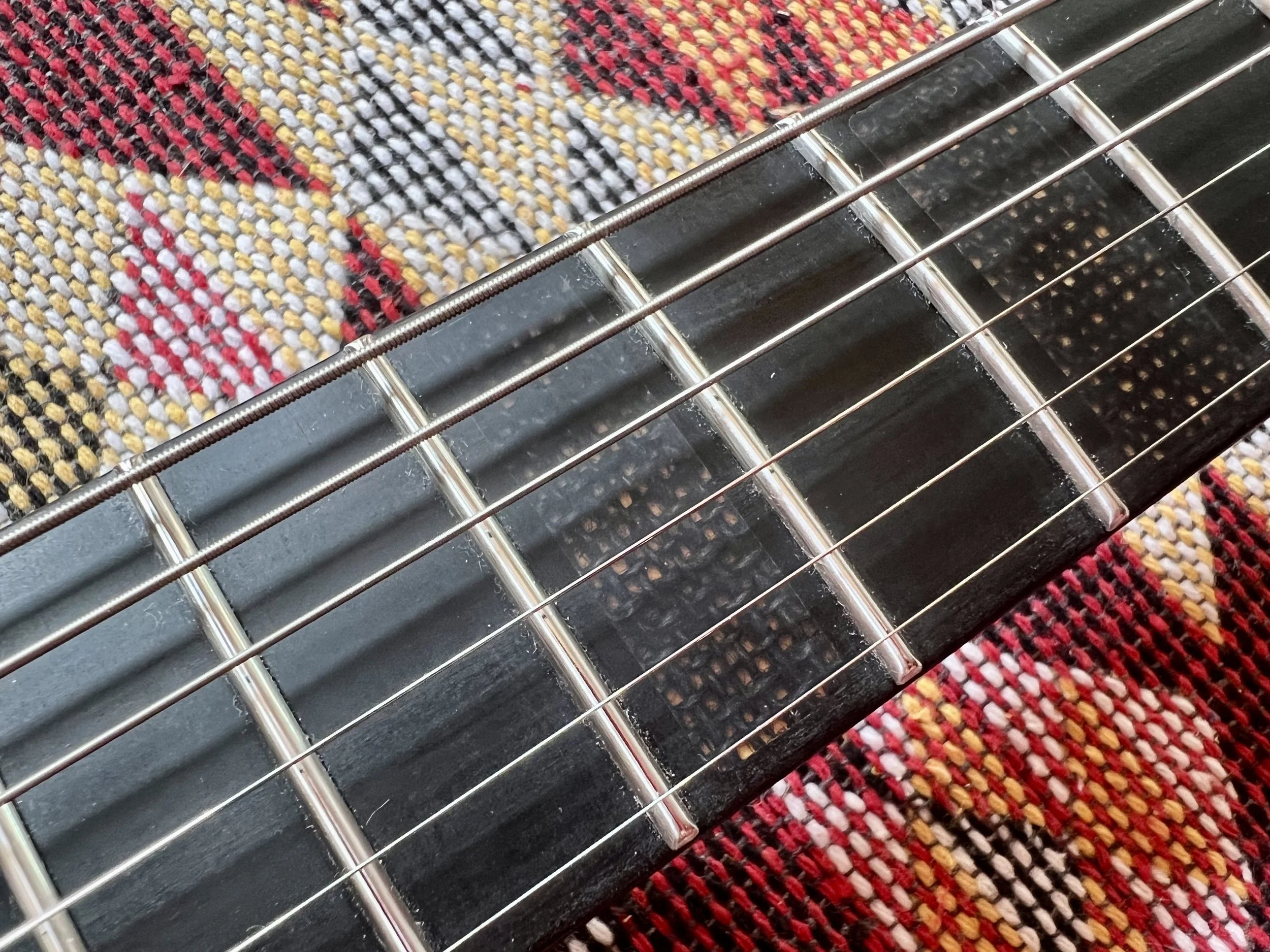 Nahaufnahme eines Gitarrenhalses mit Saiten auf einem bunten Stoff.
