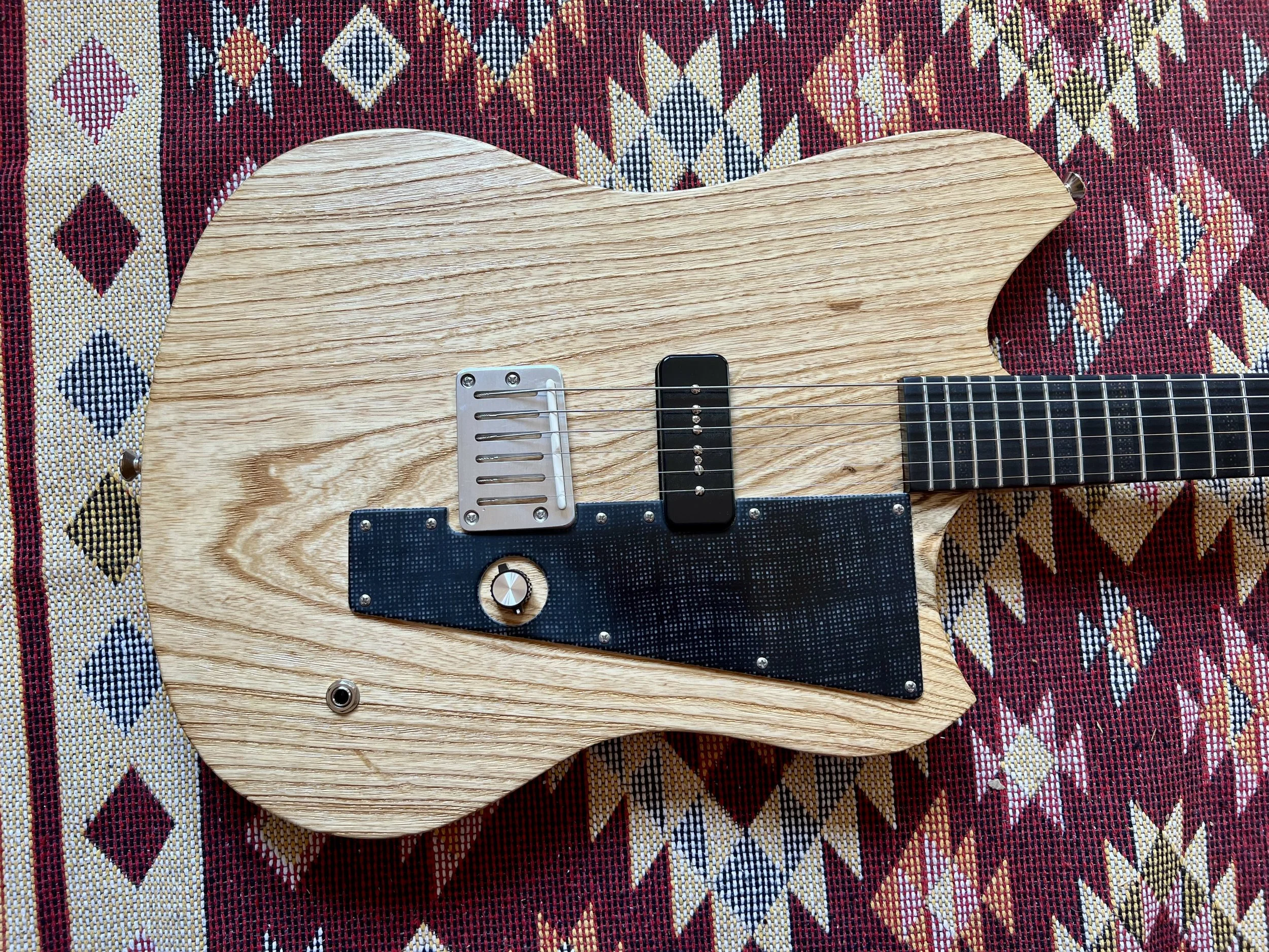 Ein holzener E-Gitarren-Korpus auf einem bunten, geometrischen Stoffmuster.