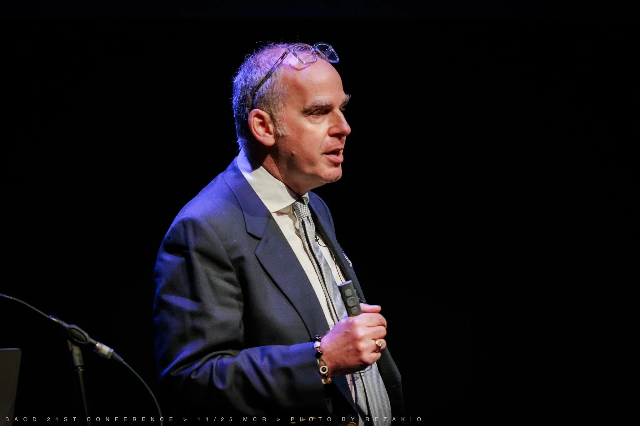 Jason speaking on stage at a conference lecture talking about crown preps holding speaker slides wearing microphone