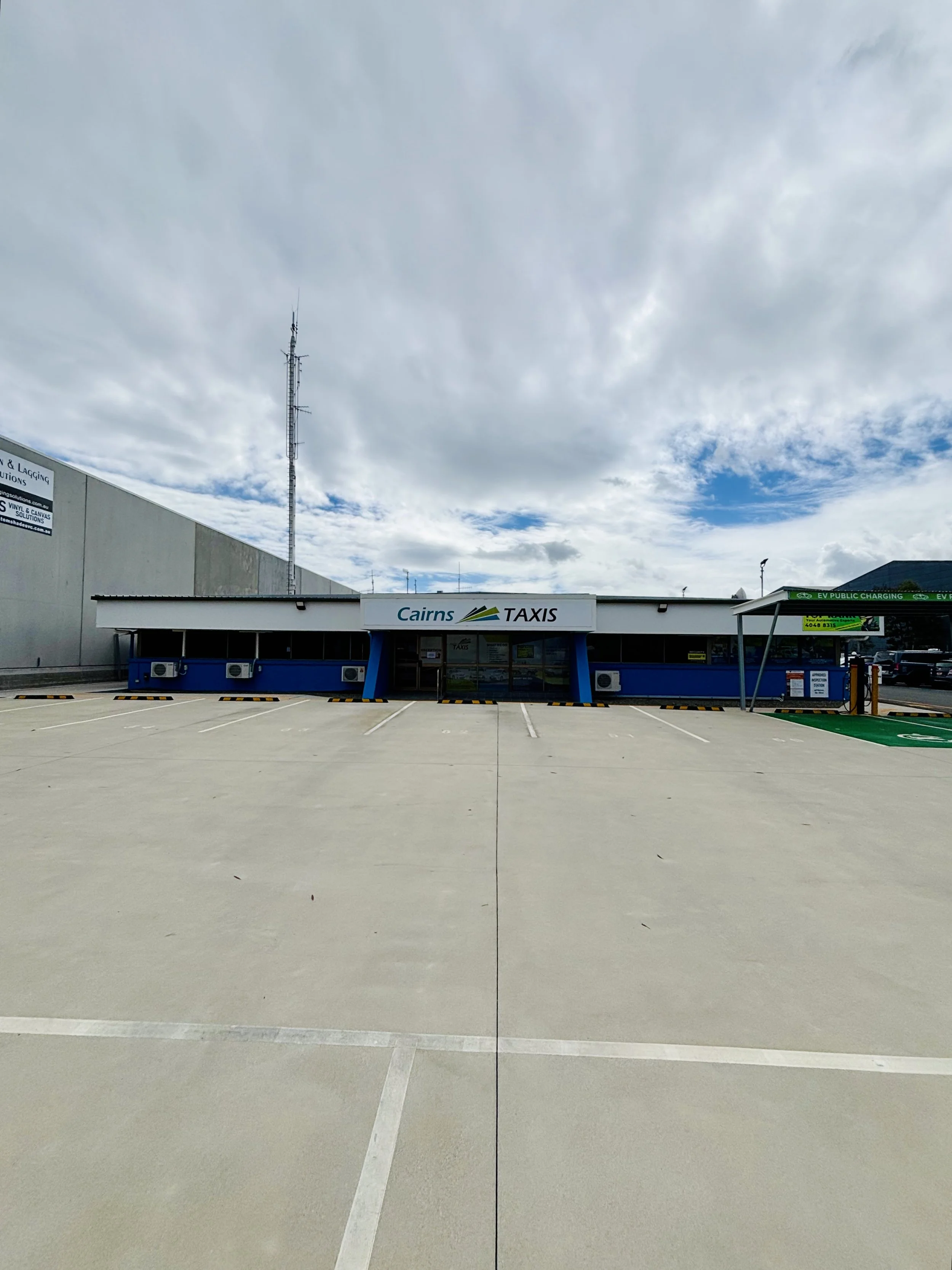 Empty parking lot in front of a building with Cairns Taxis signage, under a cloudy sky.
