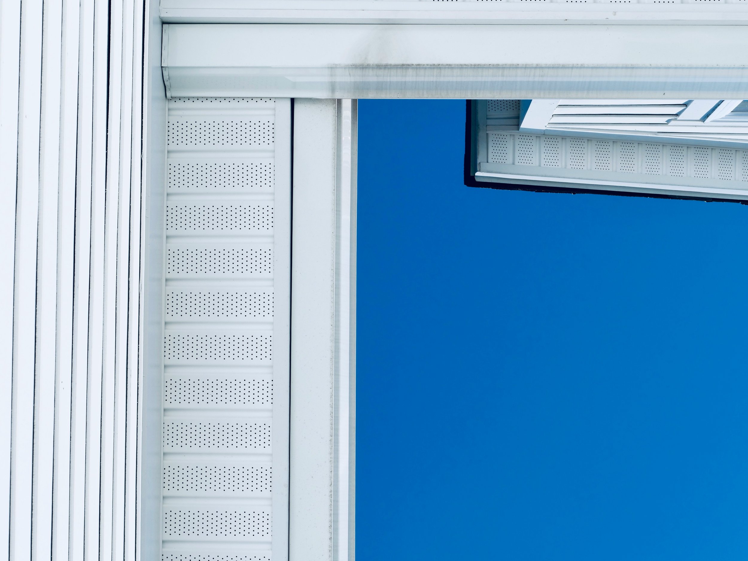 Close-up of white building siding and soffit against a clear blue sky.
