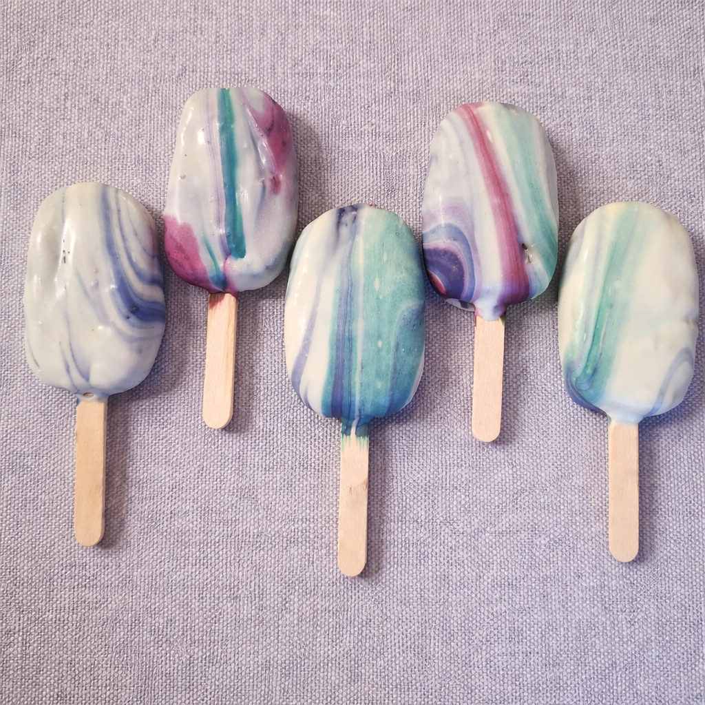 Five colorful marbled cakesicles on a soft fabric background.