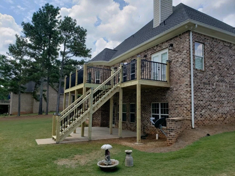 Backyard with a brick house, wooden deck, and stairs. A grassy area with a decorative bird fountain and a small statue in the foreground.
