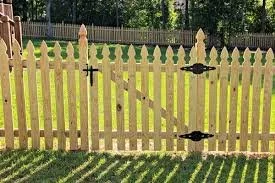 Wooden picket fence with a latch and a gate, grass lawn in front, trees behind.