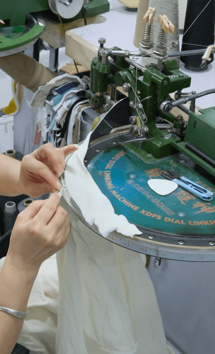 A white knitted garment being assembled on a linking machine, showing one of the key finishing steps in sweater production.