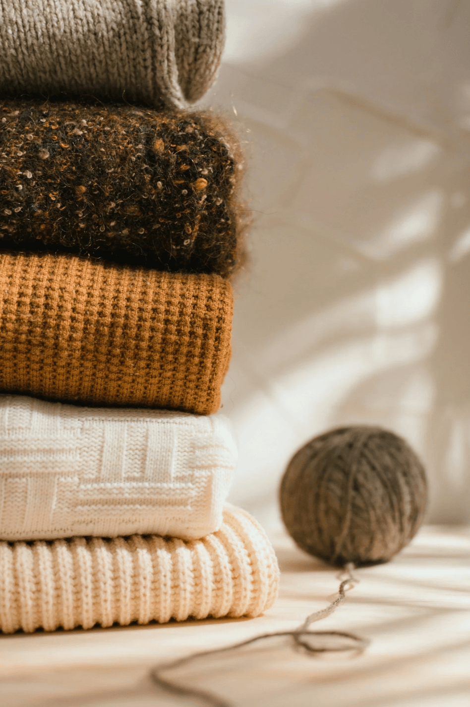 Folded knitwear samples and yarn arranged in warm neutral tones, highlighting texture, material direction, and sweater development references.
