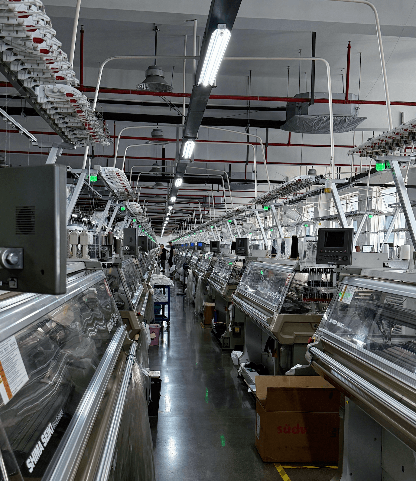 Rows of computerized flat knitting machines inside a knitwear production workshop, showing the manufacturing environment behind small-batch sweater sourcing.
