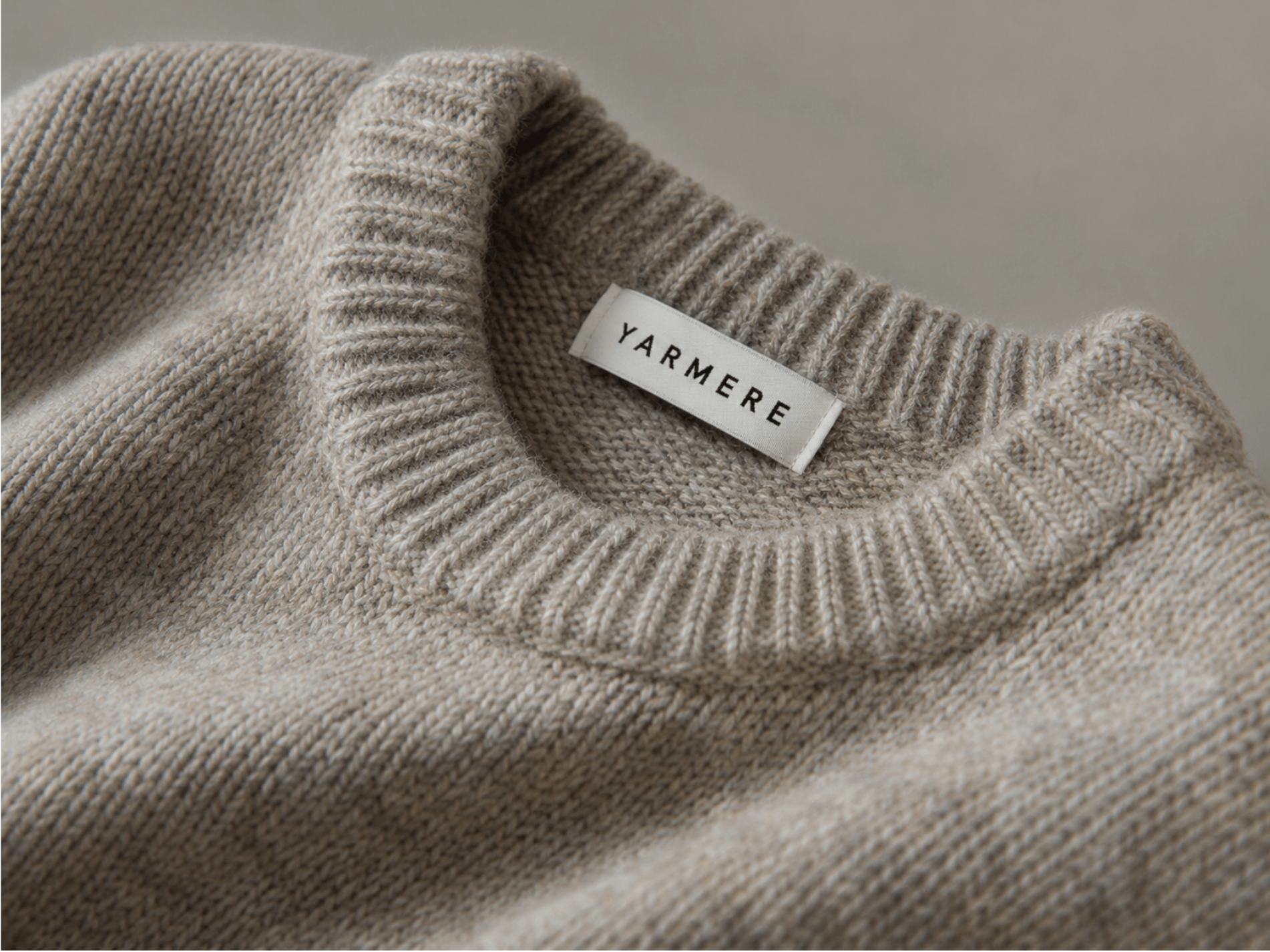 Beige knitted sweater with a ribbed neckline and label detail, showing private label knitwear finishing.