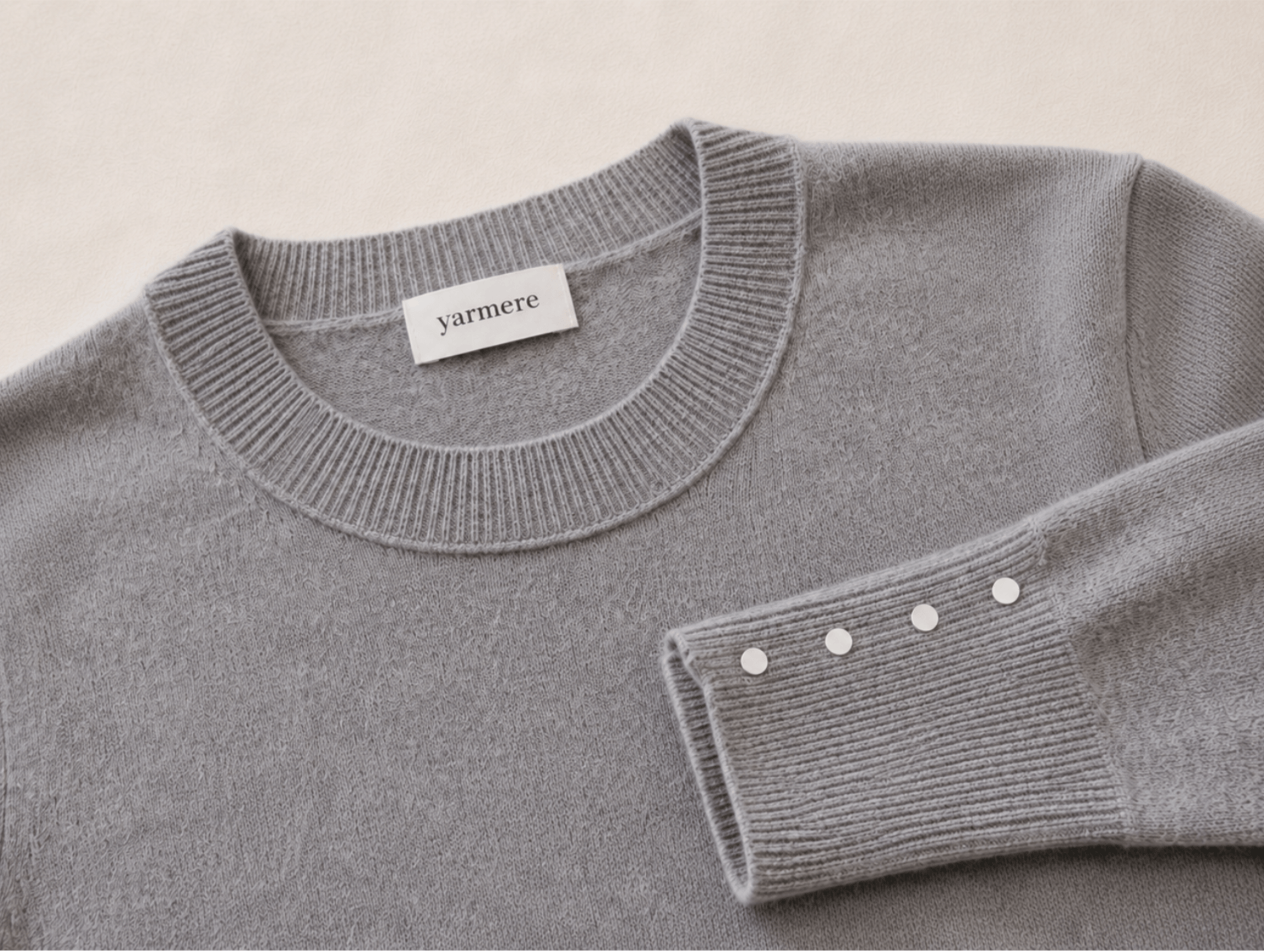 Close-up of a grey knitted sweater with ribbed trims and label details, showing knitwear finishing and product development quality.