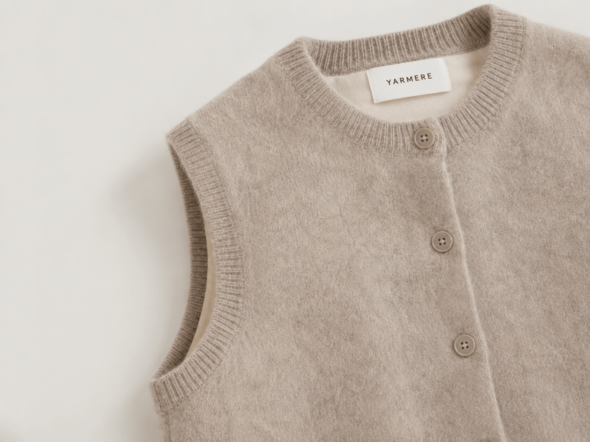 Beige knitted vest with button closure and ribbed trims, showing a small-batch knitwear style for boutique brand development.