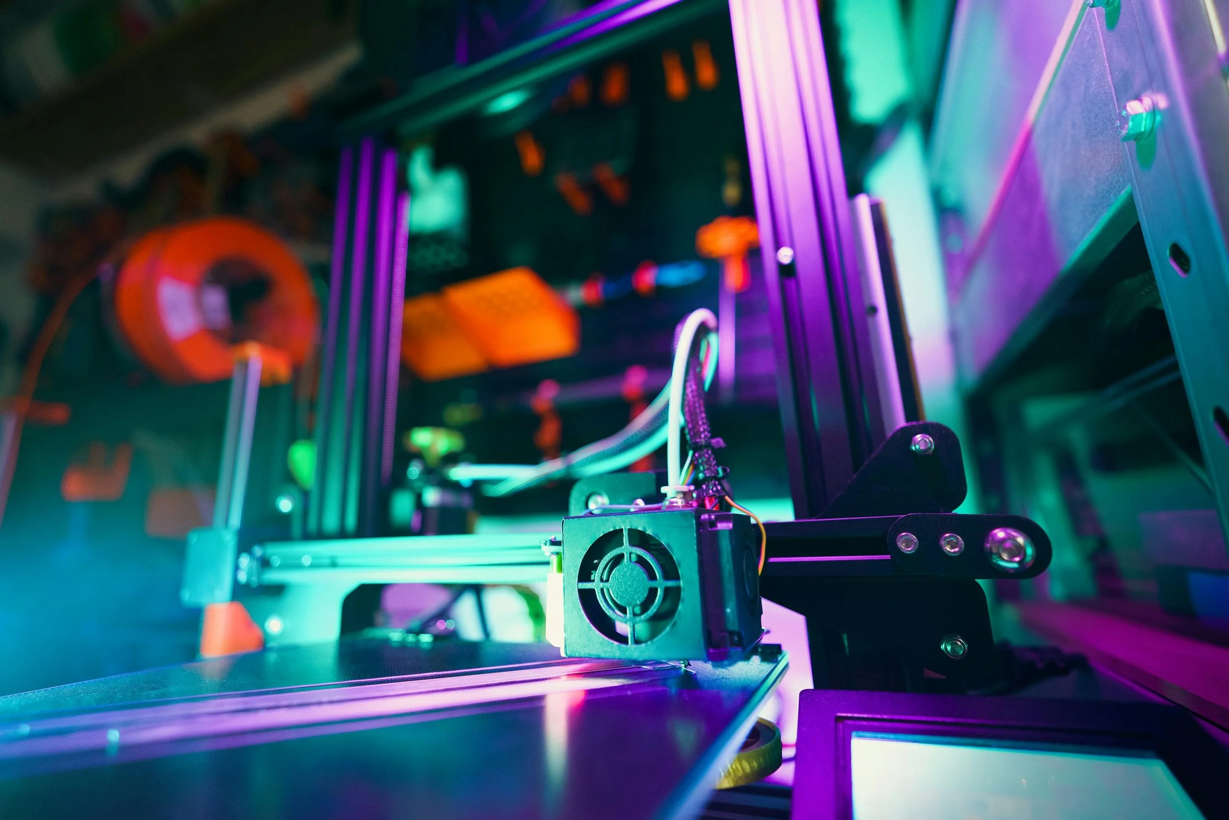Vista di una stampante 3D con luci a LED di vari colori, componenti meccanici e circuiti visibili, in un ambiente tecnologico.