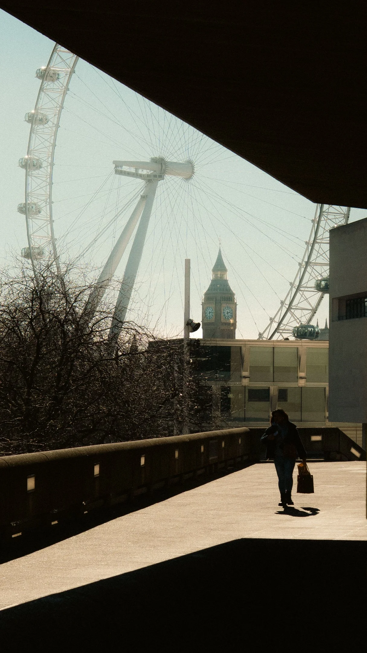 A woman walking with a suitcase on a bridge, with the London Eye and Big Ben in the background.