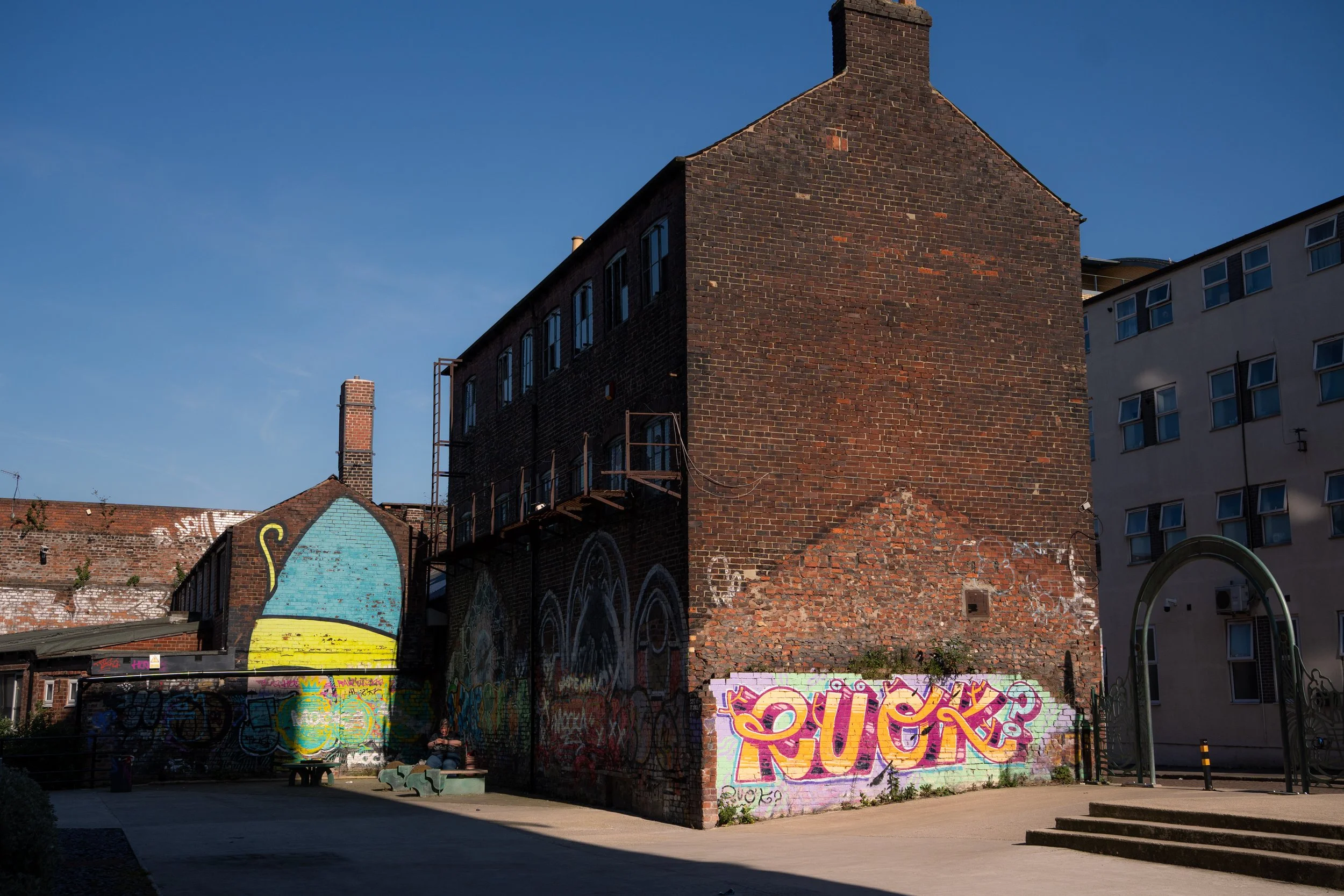 Urban scene featuring a brick building with graffiti art on the lower wall, graffiti on the building itself, and a clear blue sky.