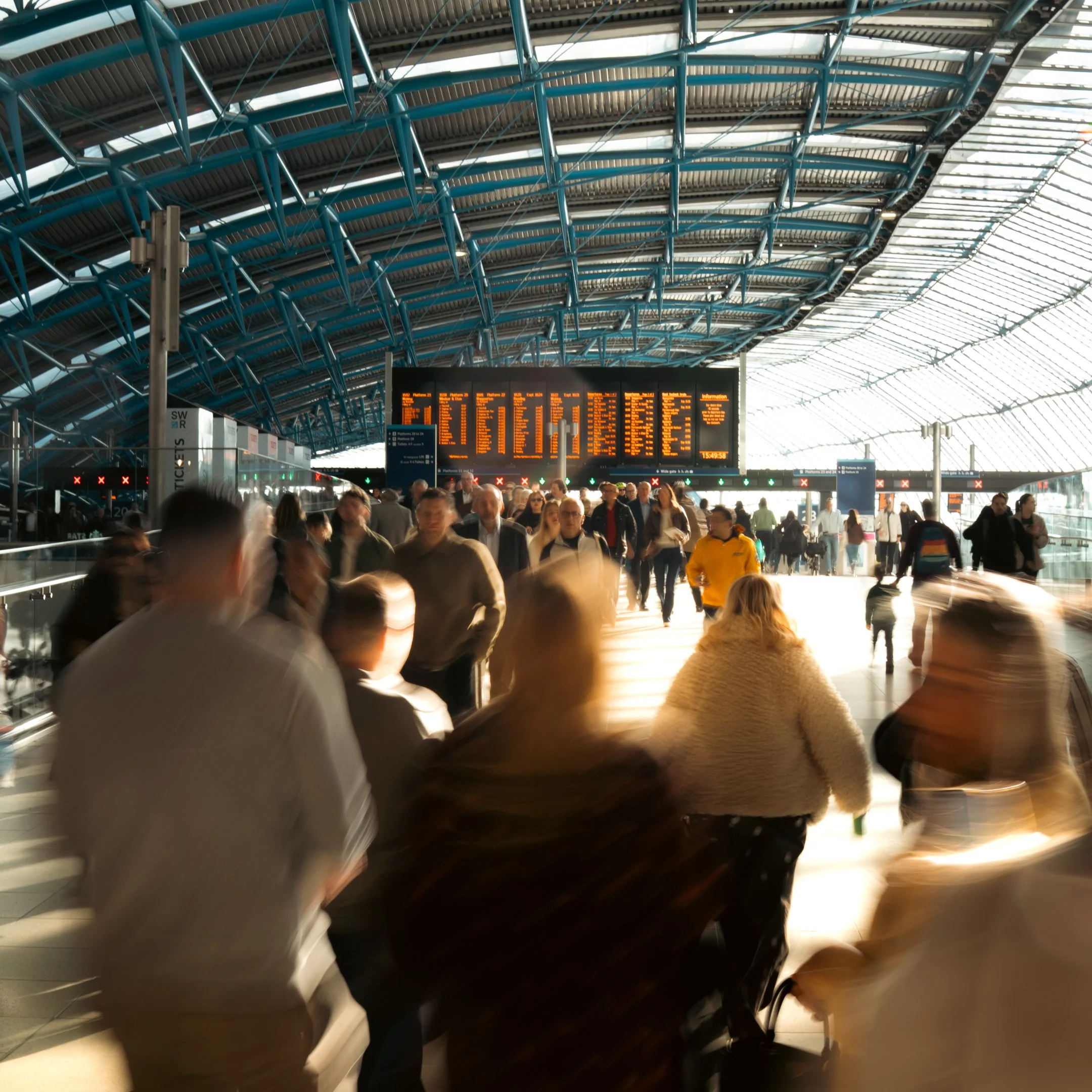 People walking through a busy airport terminal with a high arched ceiling and an electronic departure board.