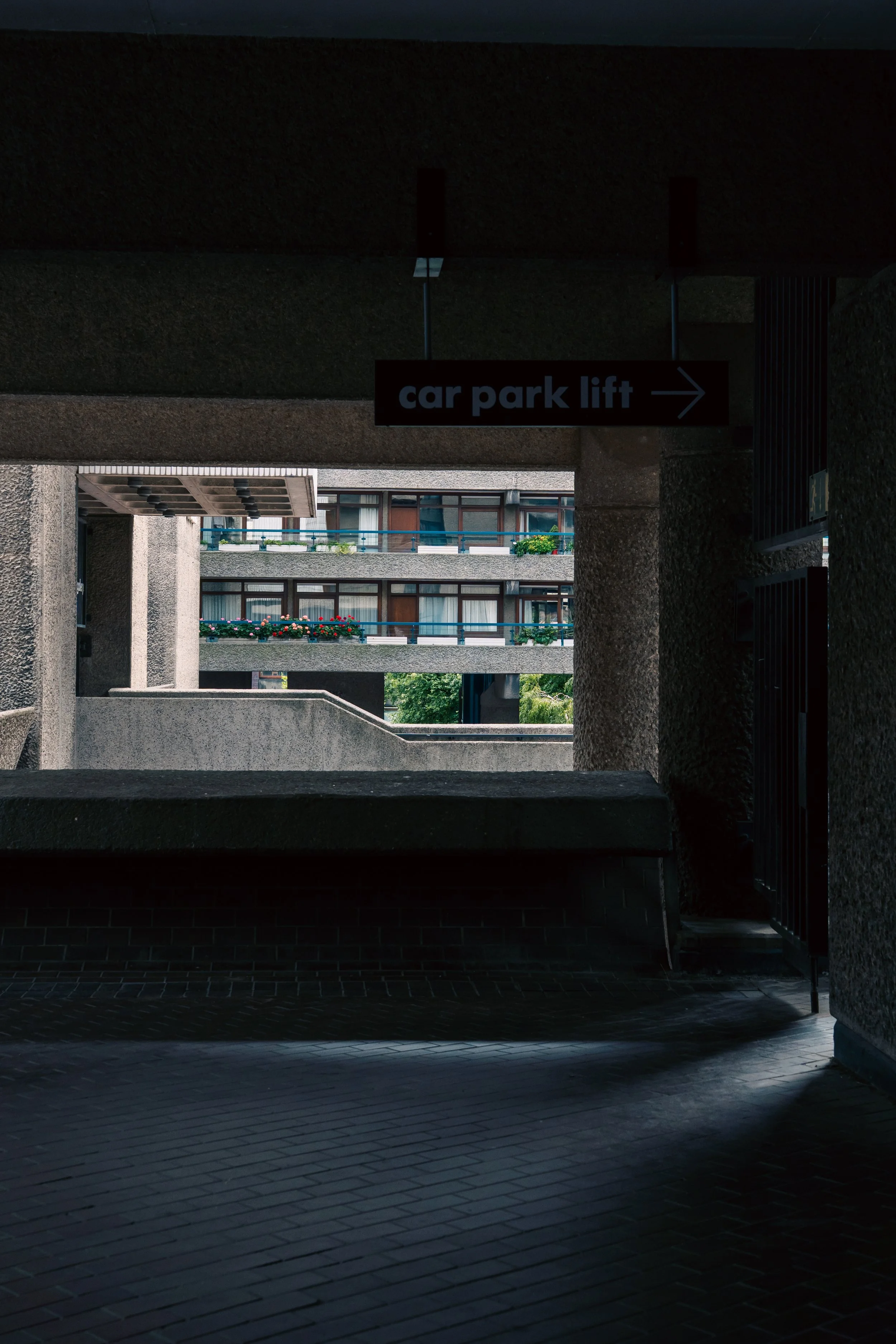 Photo of an apartment complex viewed from a parking garage, showing balconies with flower boxes and sliding glass doors.