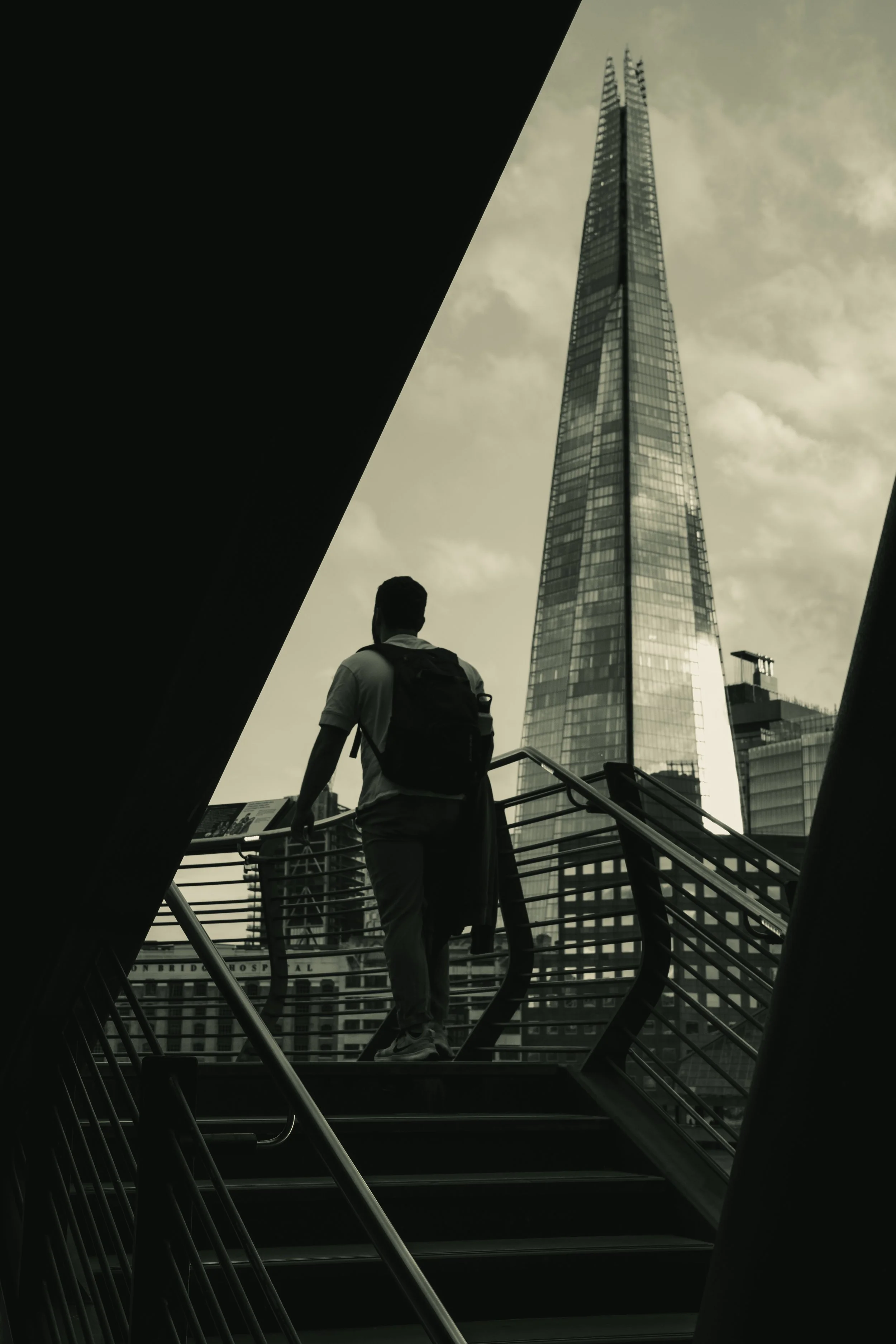 A person with a backpack walking up a staircase with the city skyline, including a tall building, in the background.