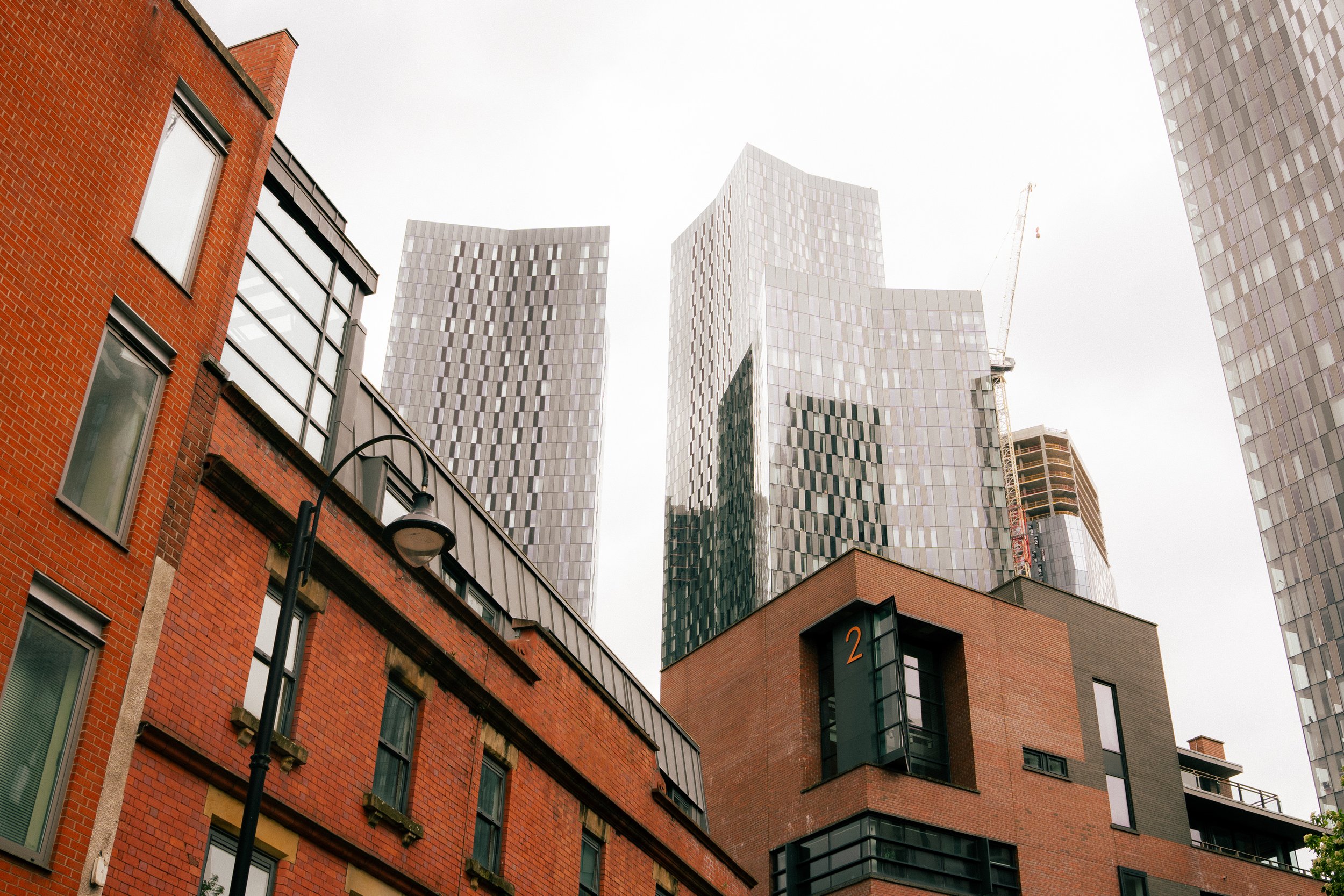 Low-angle view of modern glass skyscrapers and older brick buildings in an urban setting on a cloudy day.