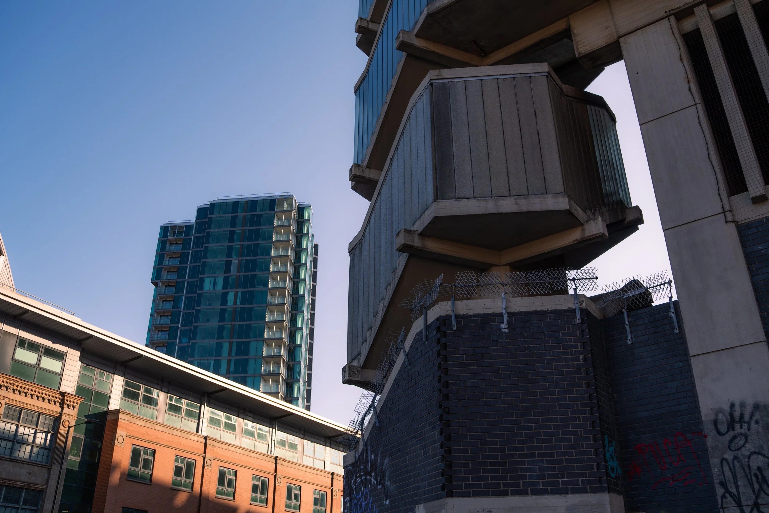 View of tall modern glass buildings alongside older brick and concrete buildings, with a clear blue sky in the background.