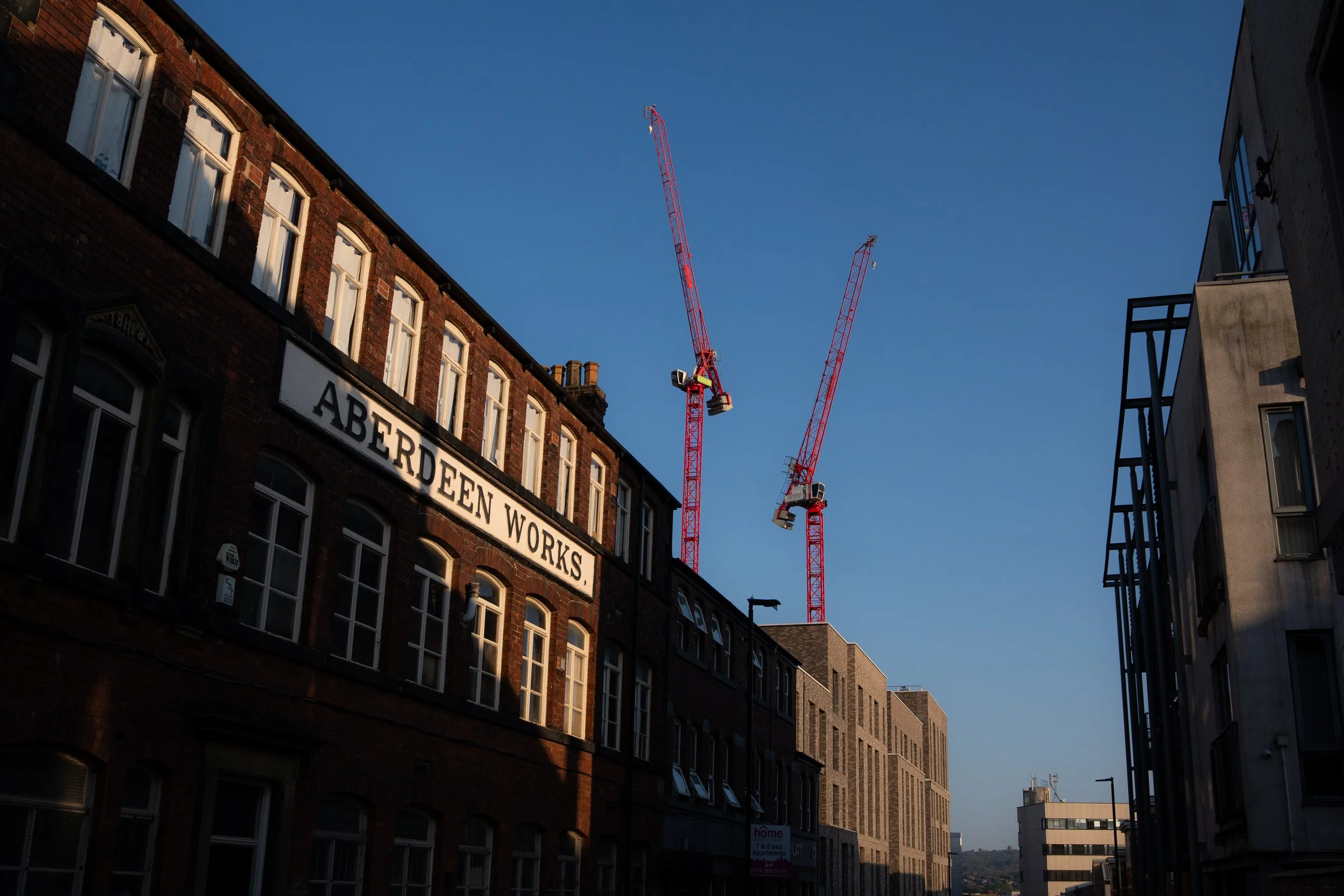 View of several buildings with a red construction crane towering above, under a clear blue sky.