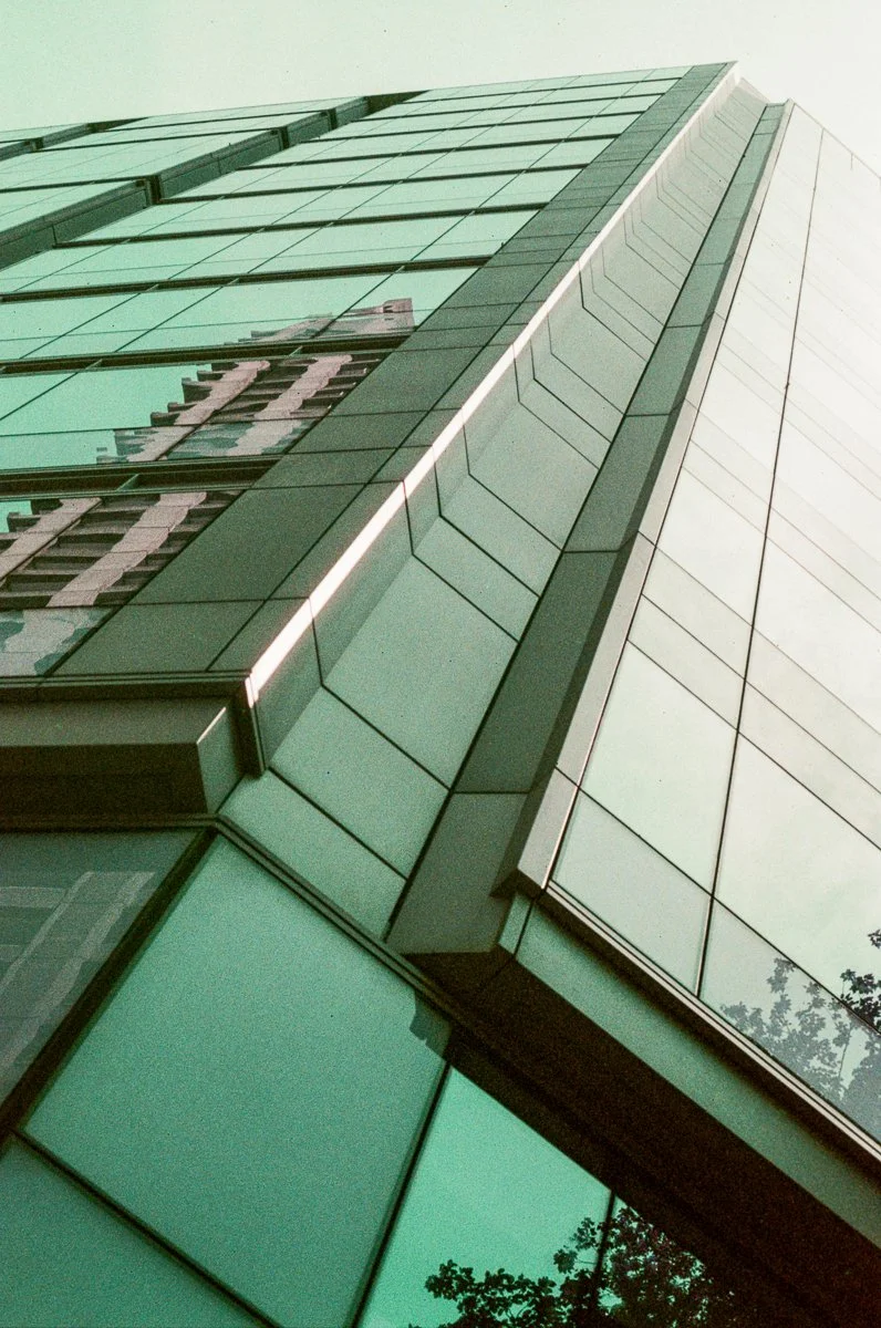 Low-angle view of a modern skyscraper with glass windows reflecting the sky and surrounding buildings.