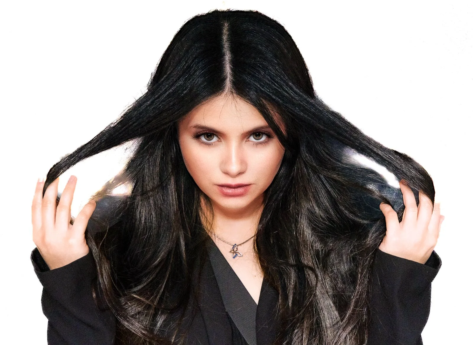 Woman with long black hair holding her hair with both hands, looking directly at the camera, wearing a black top and a necklace with a dolphin pendant, against a white background.