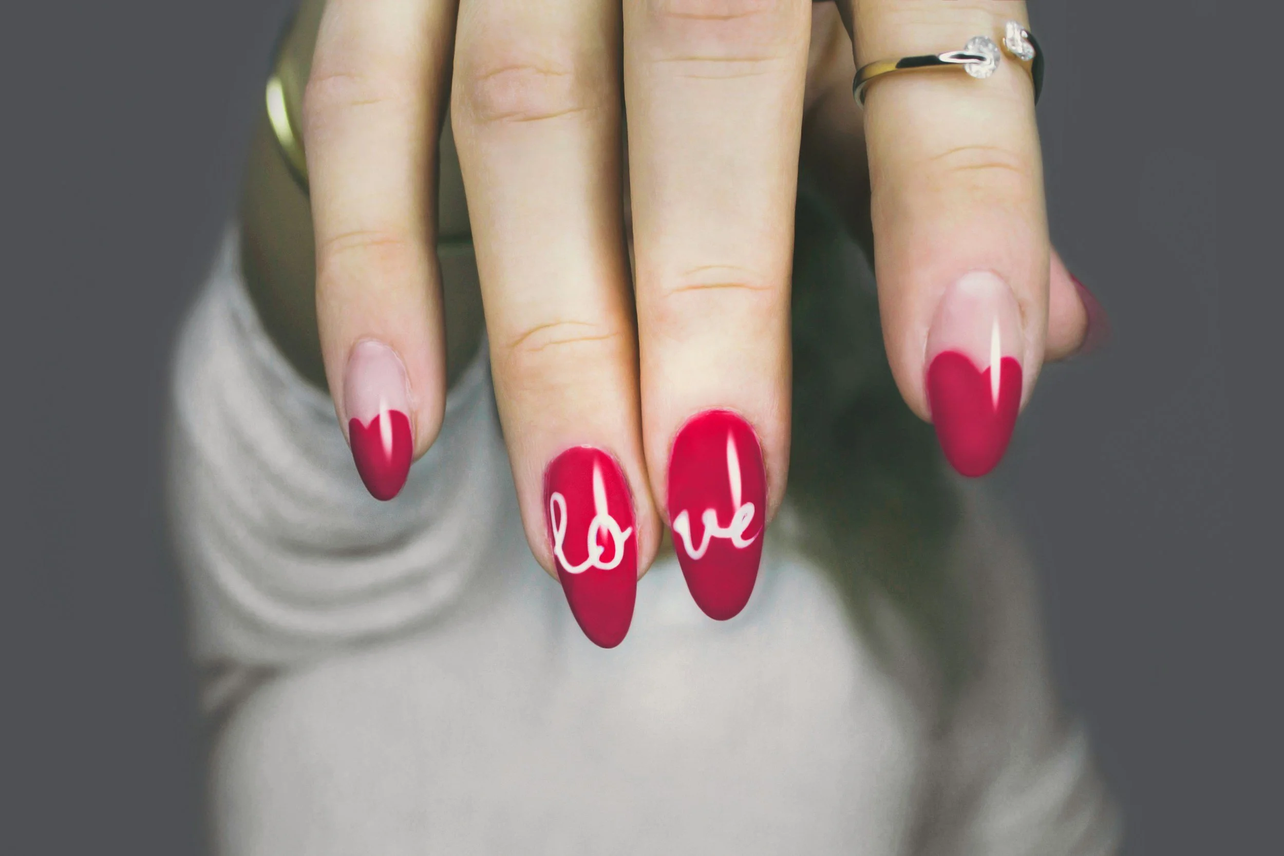 Close-up of a hand with red-painted nails, with the word 'love' written on the nails.