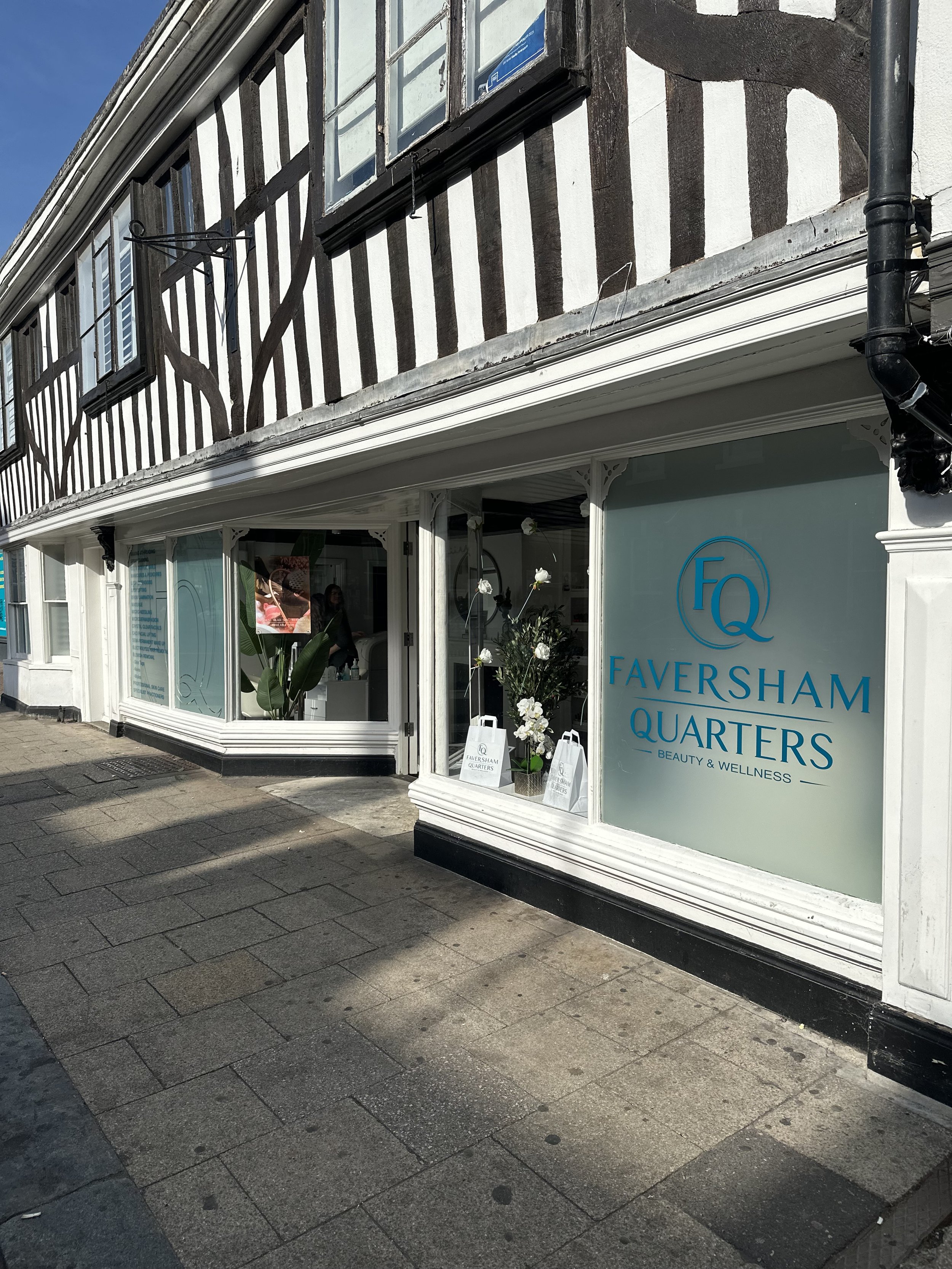 The storefront signage for Faversham Quarters, a beauty and wellness business, with large glass windows and a display of white orchids outside, on a city sidewalk with wet pavement.