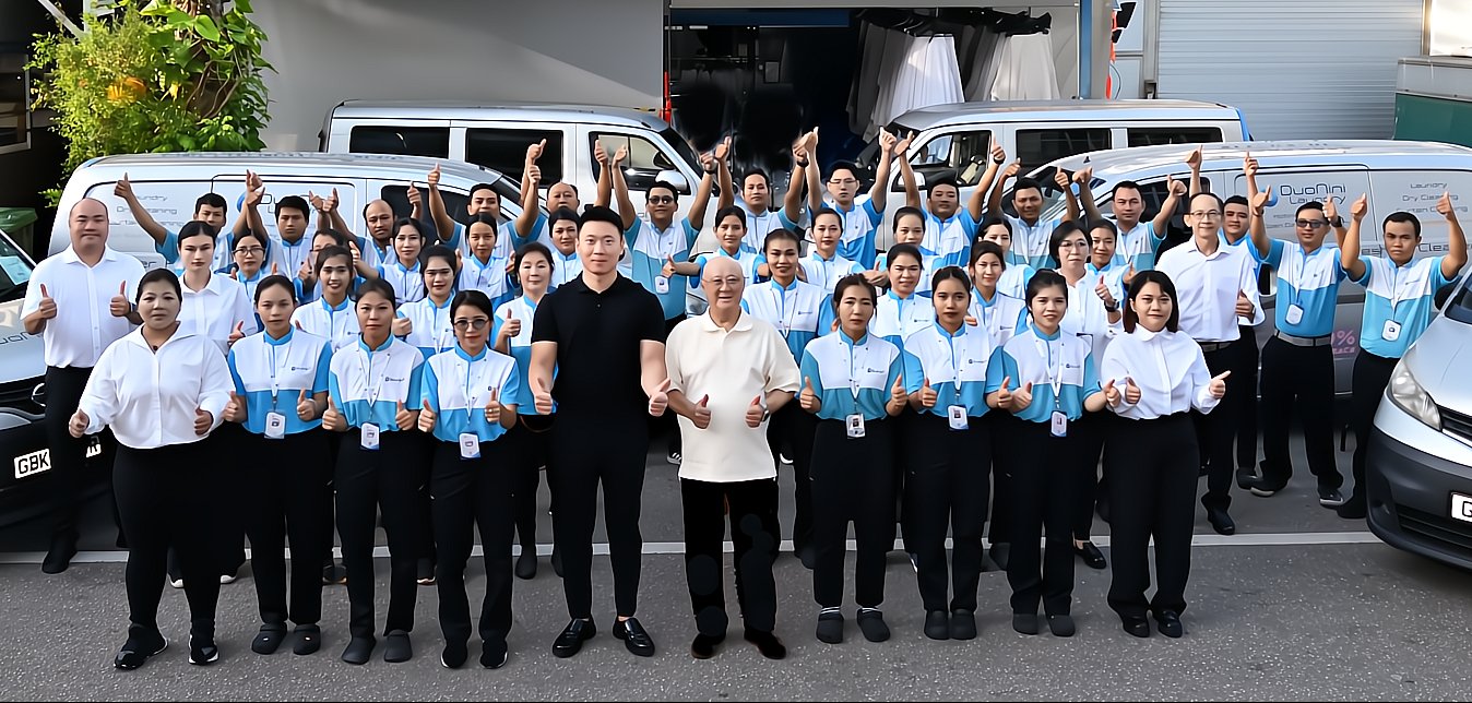 Group of employees posing together outside in front of company vehicles, giving thumbs up gesture