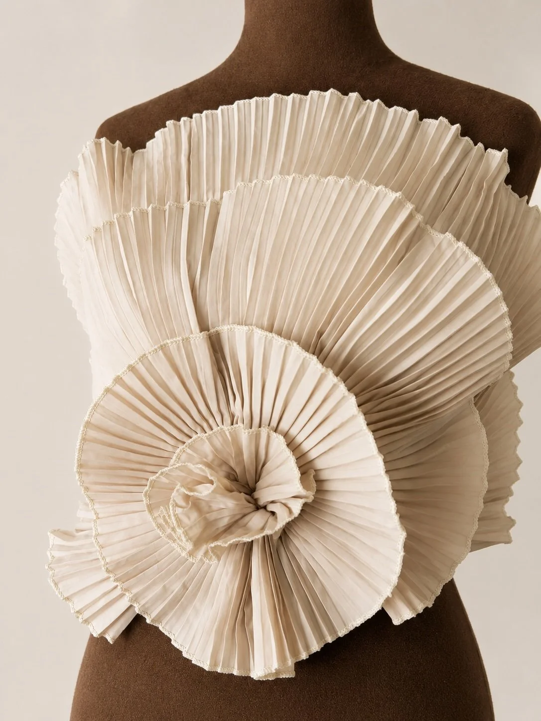 An abstract sculpture made of pleated, cream-colored fabric arranged in a spiral pattern on a mannequin torso.
