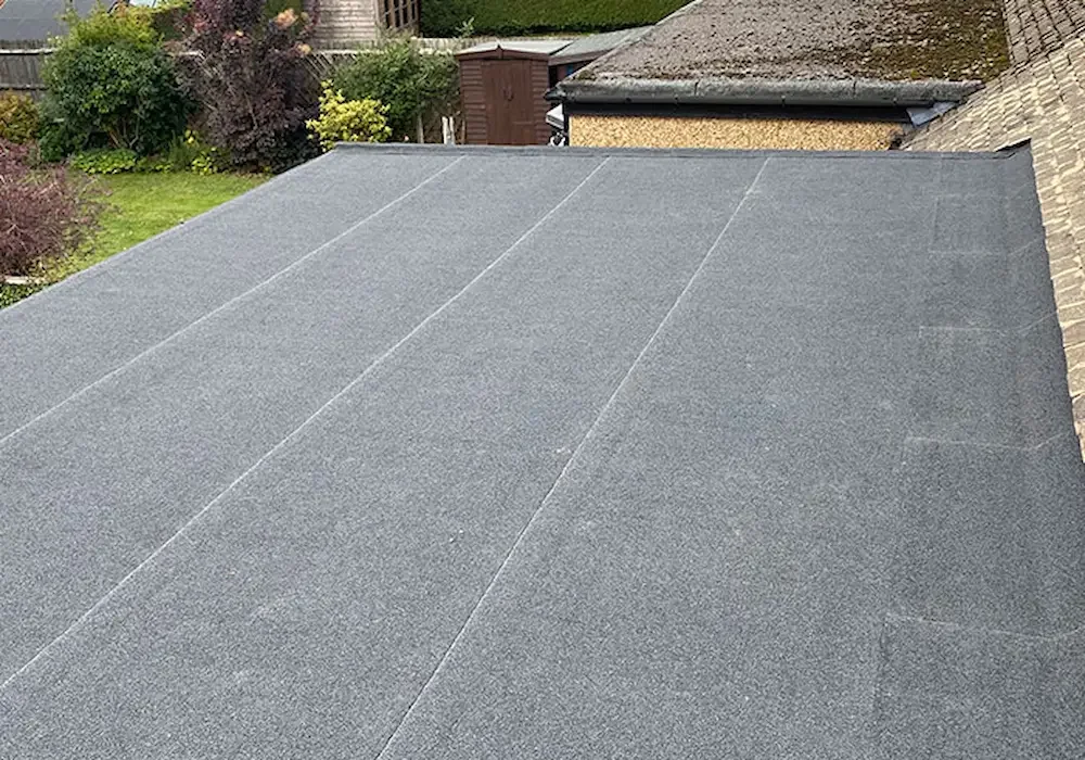 A roof with grey felt or membrane roofing material, with visible seams, extending from a brick building to a shed or extension on the right.