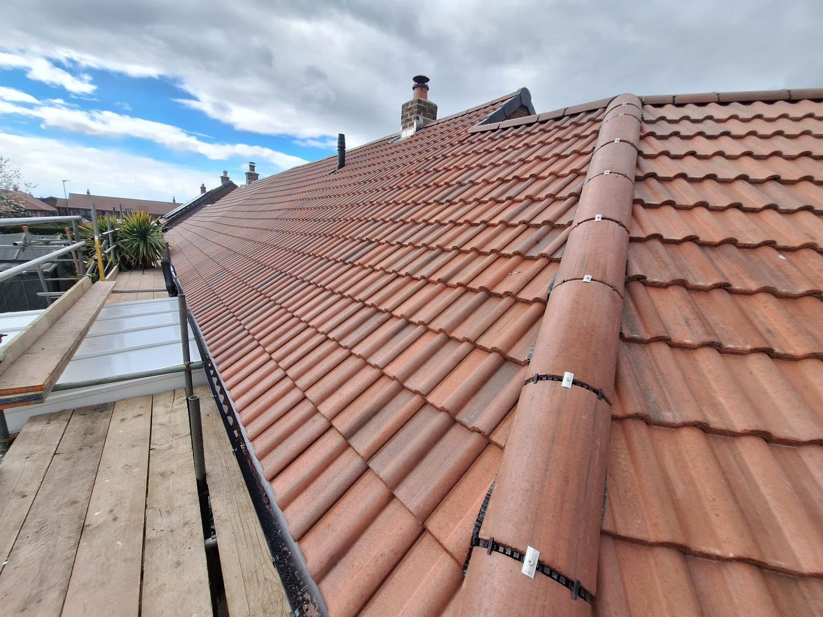 A roof with clay tiles and a section of scaffolding on the side, with cloudy skies overhead.