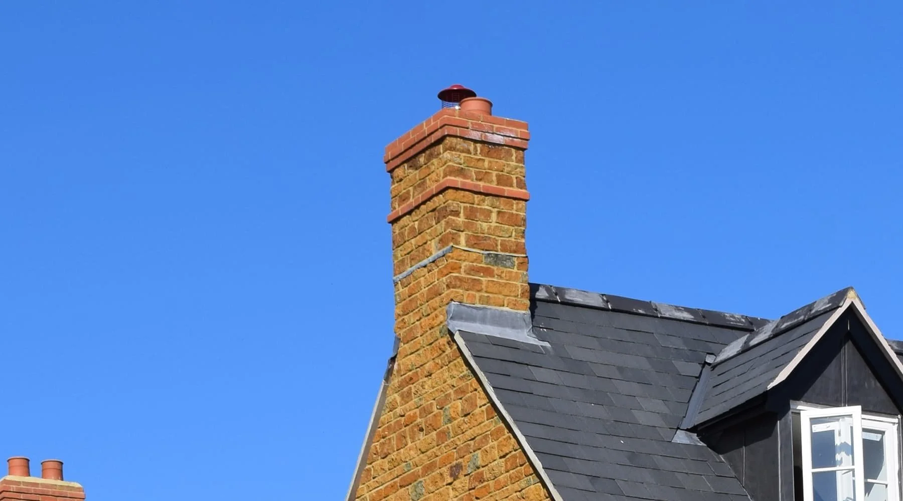 Close-up of a brick chimney on a house with a blue sky background.