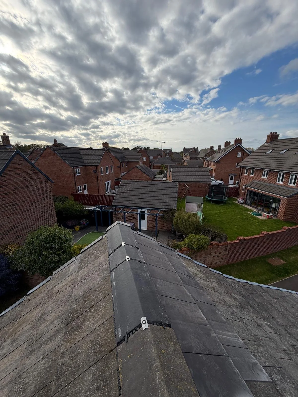 View from a rooftop overlooking rows of brick houses with gardens and a cloudy sky overhead.