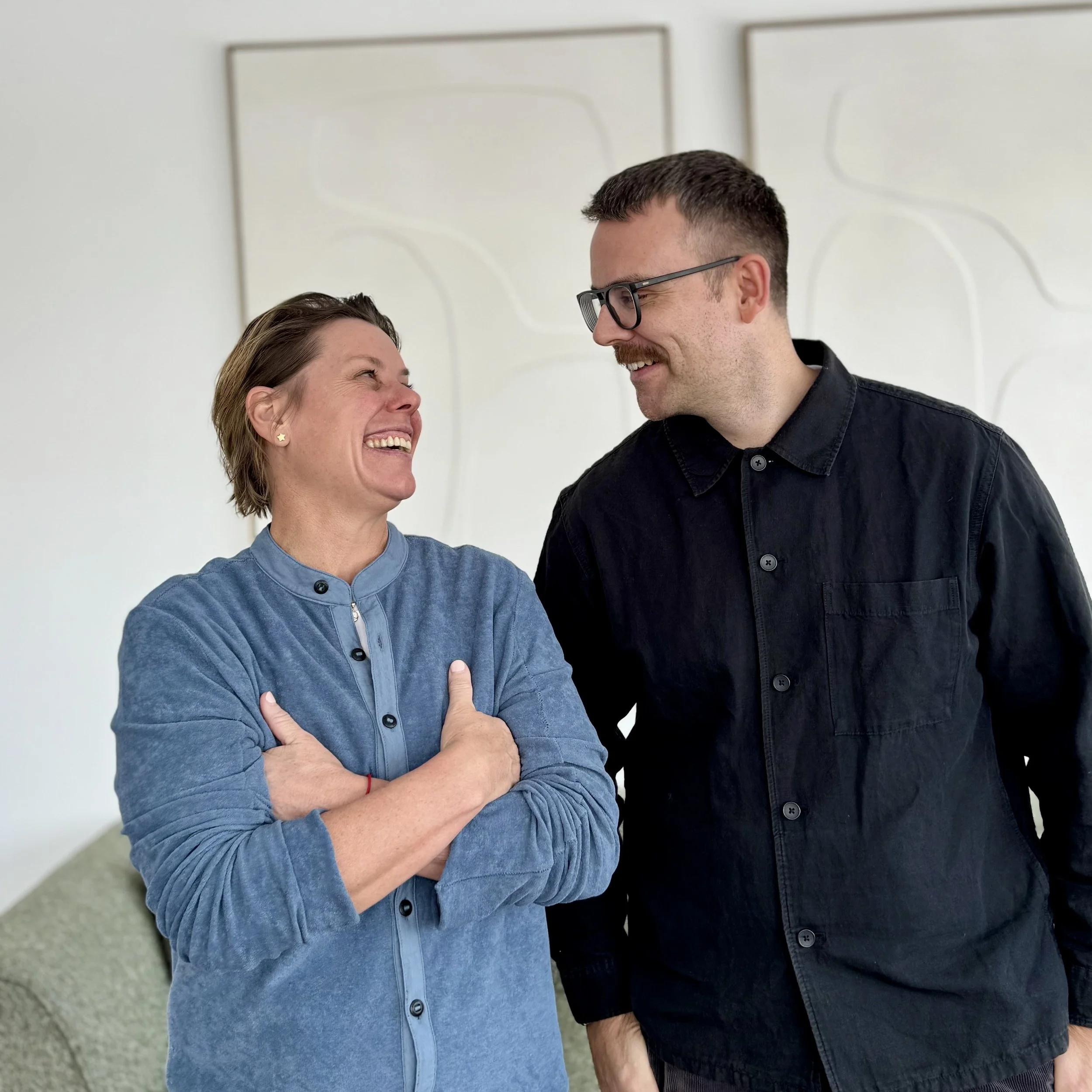 Zwei Menschen stehen sich gegenüber, lachen und haben Spaß, in einer hellen, modernen Umgebung.