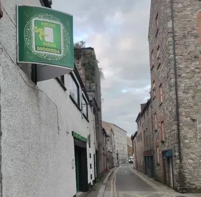 Empty narrow street with old stone buildings on the sides and a green sign for a hostel on the left. Loation of Escape RoomsDrogheda.